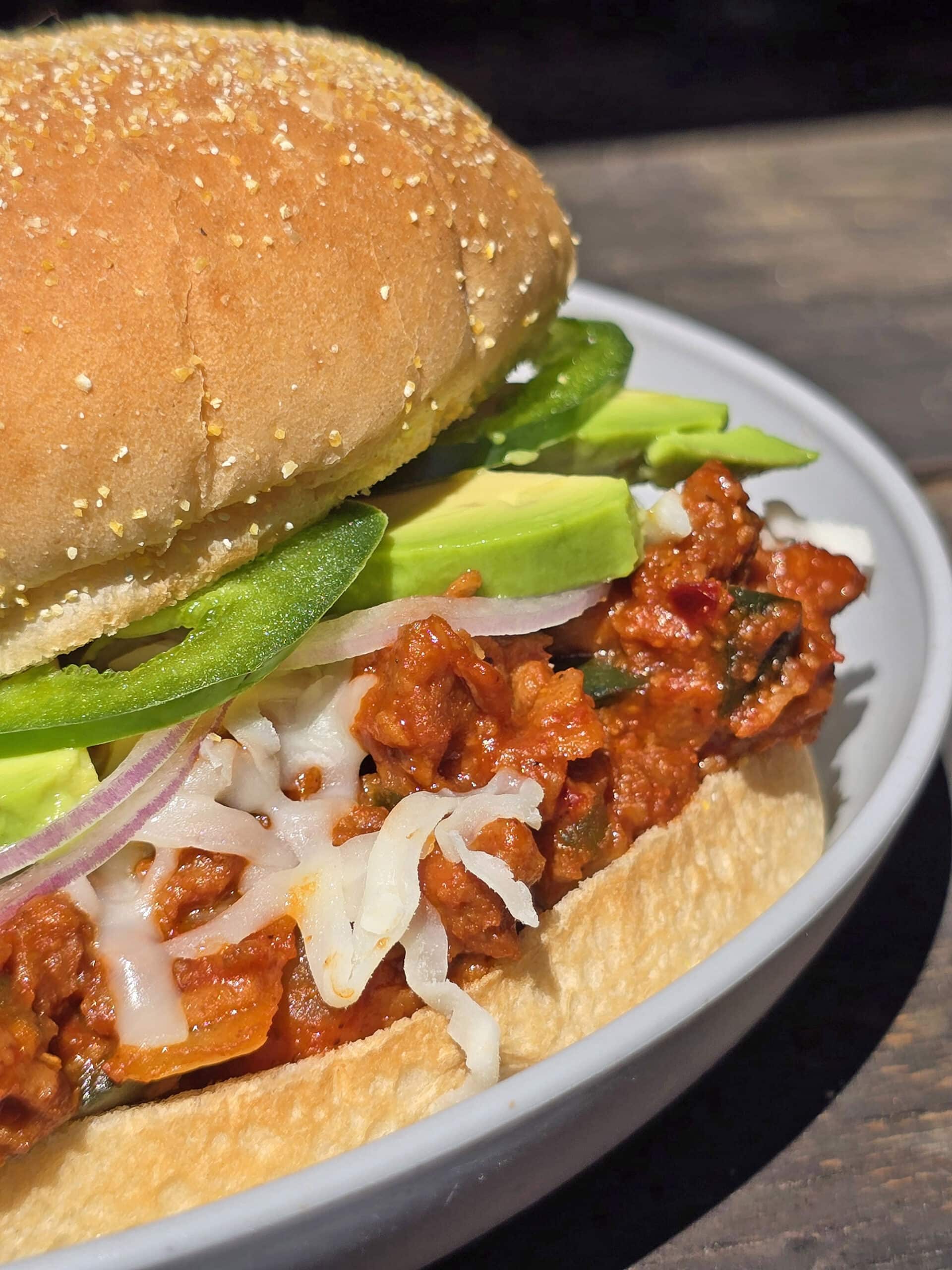 A Mexican sloppy Jose sandwich, with Monterey Jack, sliced jalapenos, and avocado, on a plate.