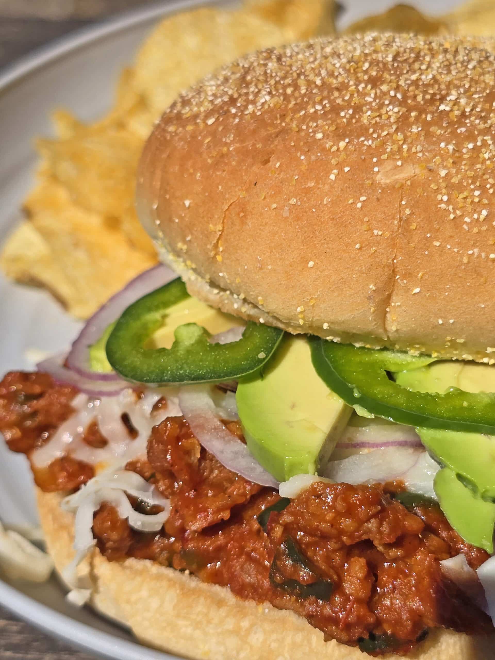 A Mexican sloppy Joe sandwich, with Monterey Jack, sliced jalapenos, and avocado, on a plate.