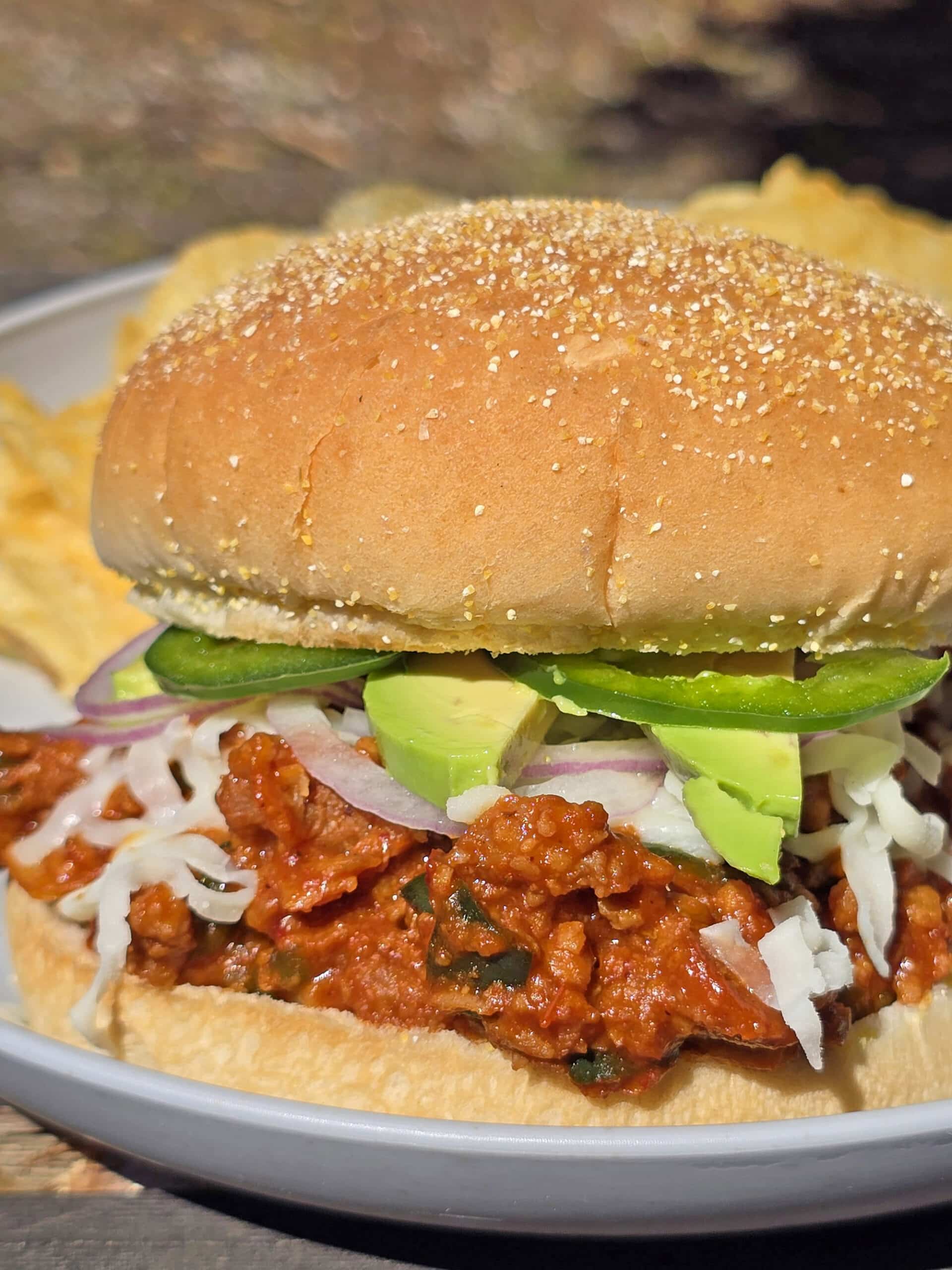 A Mexican sloppy Jose sandwich, with Monterey Jack, sliced jalapenos, and avocado, on a plate.