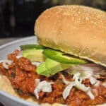 A Mexican sloppy Joe sandwich, with Monterey Jack, sliced jalapenos, and avocado, on a plate.