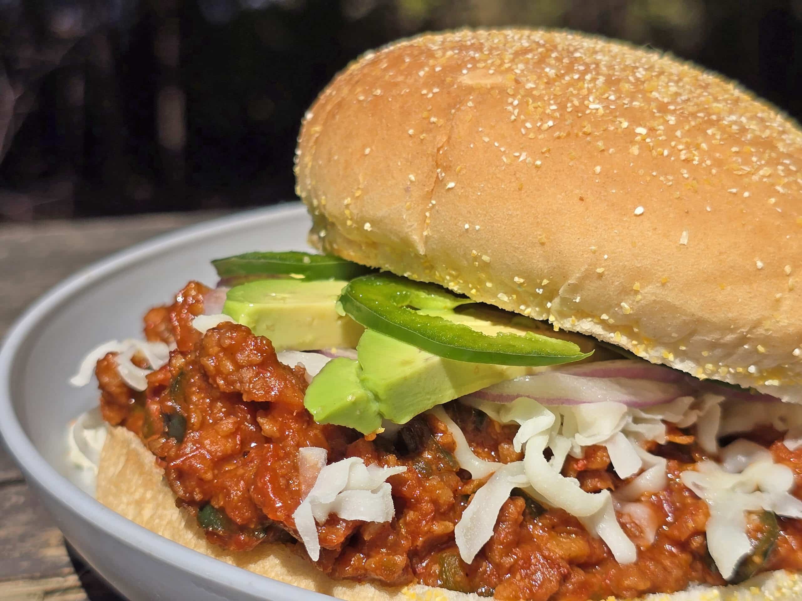 A Mexican sloppy Joe sandwich, with Monterey Jack, sliced jalapenos, and avocado, on a plate.