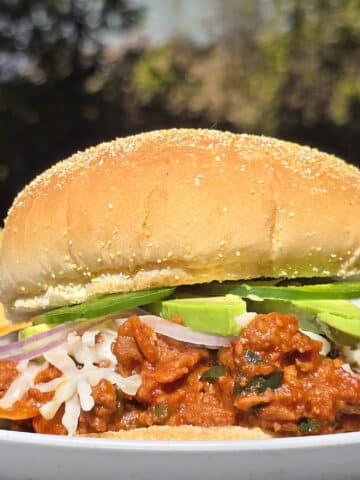 A Mexican sloppy Jose sandwich, with Monterey Jack, sliced jalapenos, and avocado, on a plate.