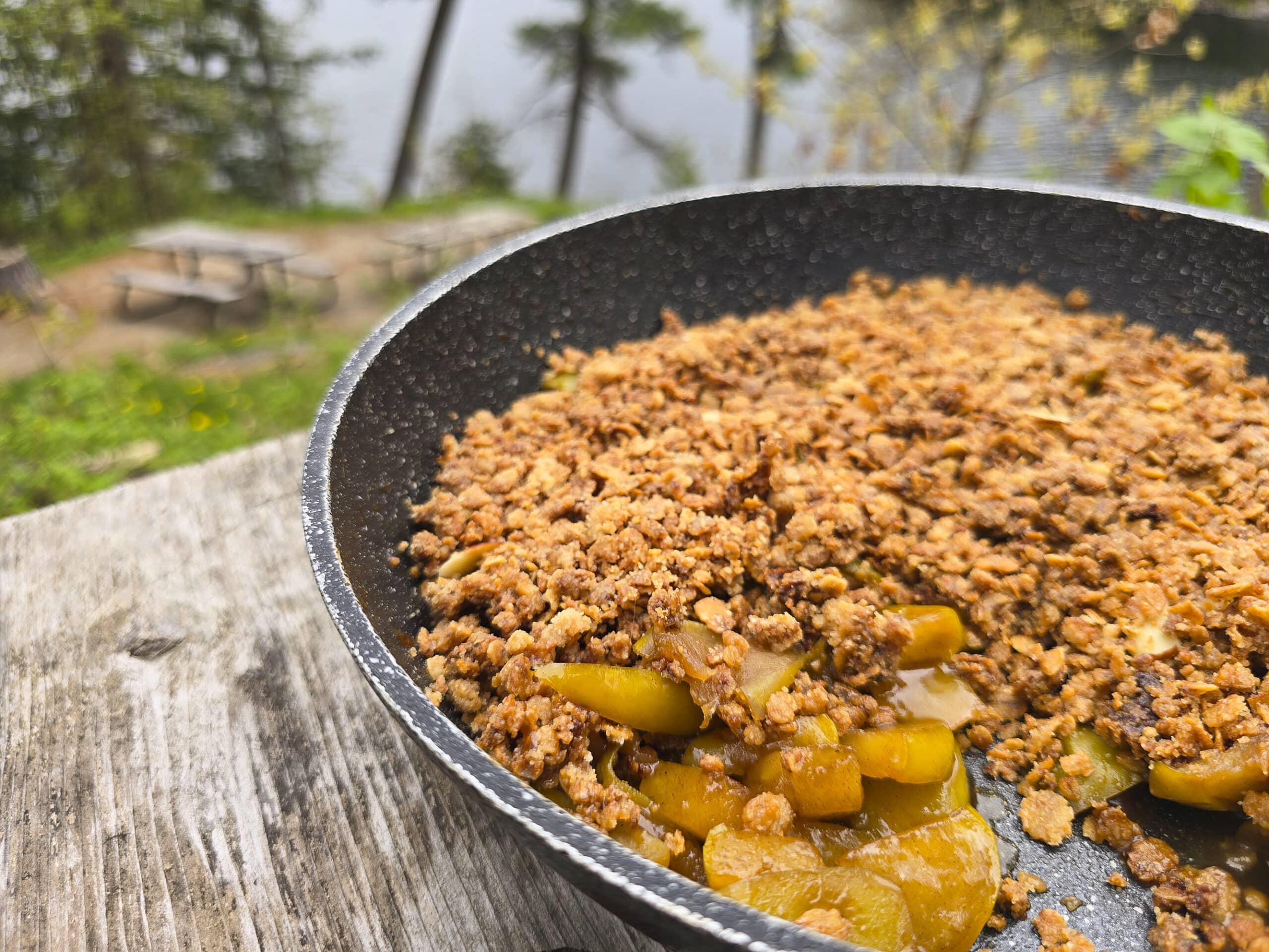 A skillet of apple crisp on a picnic table.