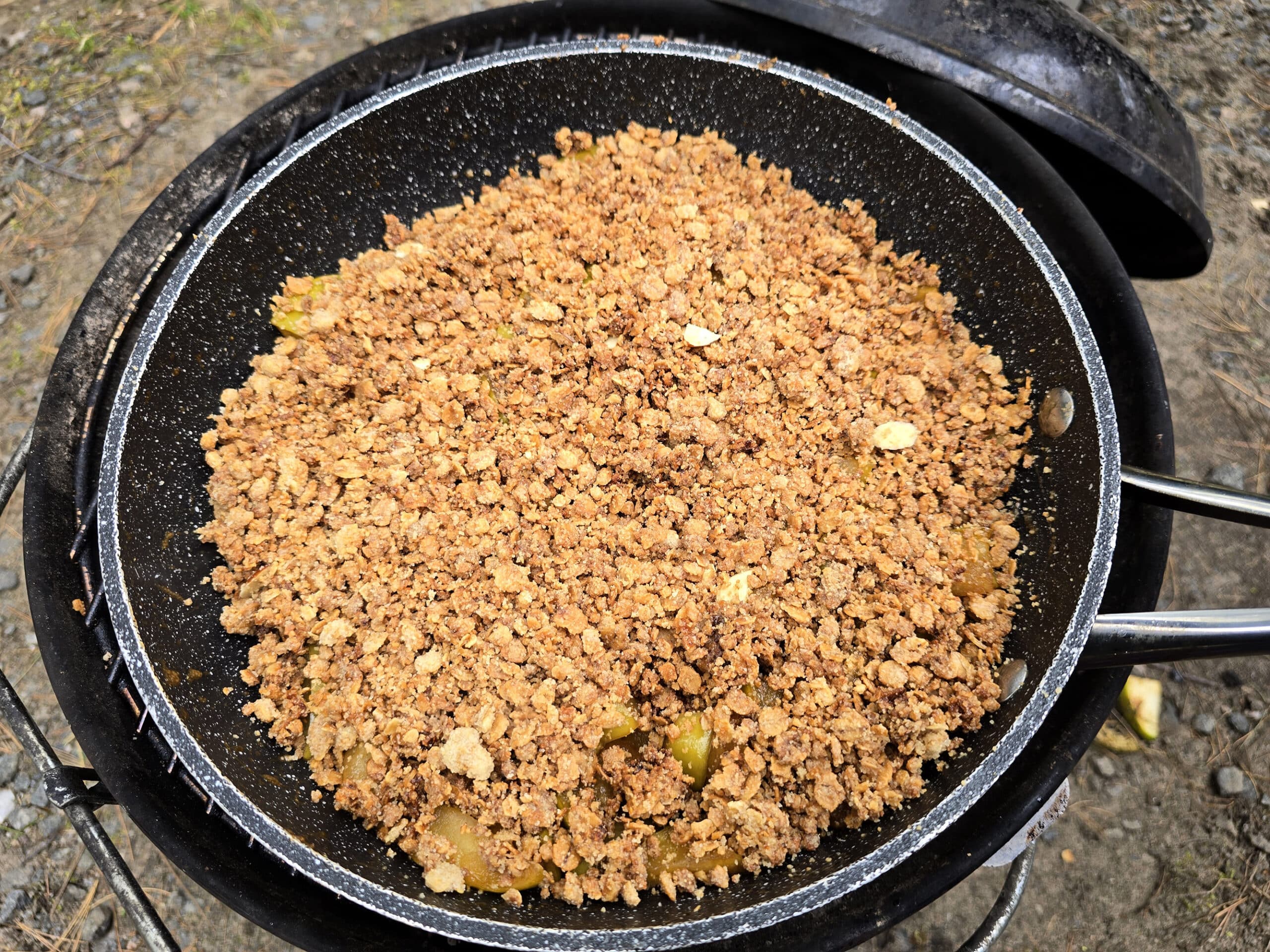 A skillet of apple crisp on a charcoal grill.