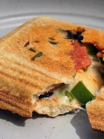 A pizza pudgy pie on a plate, filled with mozzarella, green peppers, pepperoni, and black olives.