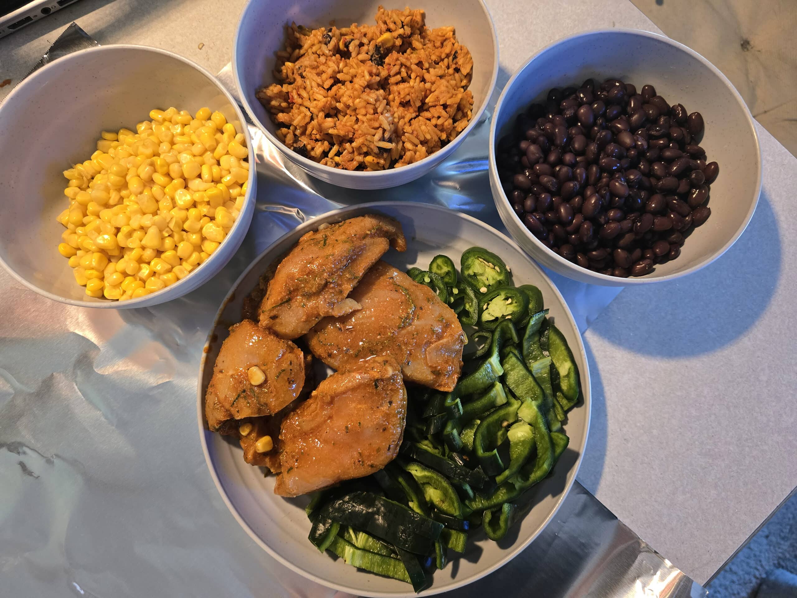 Bowls of corn, Mexican rice, black beans, marinated chicken breast, and peppers.