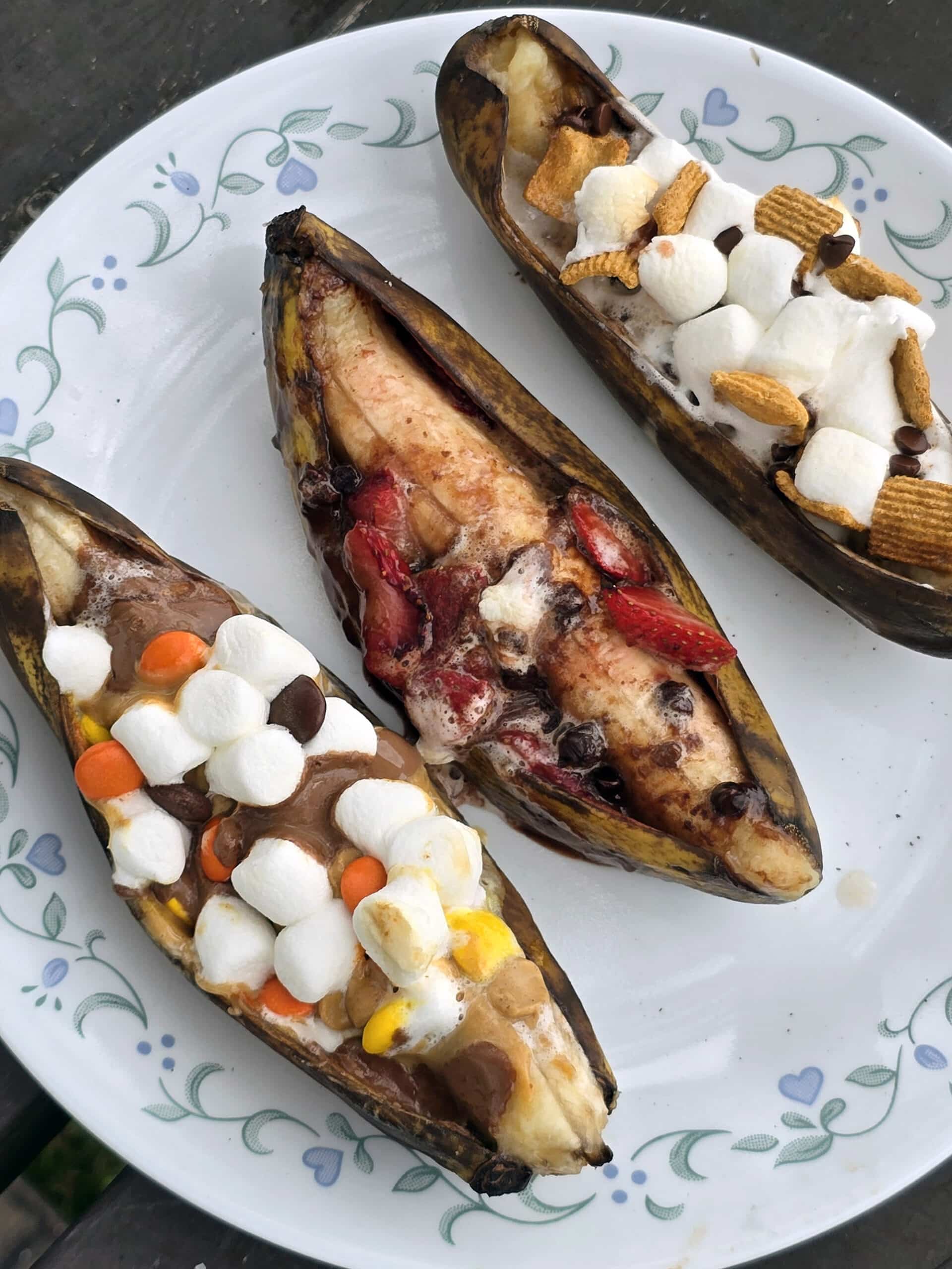 3 grilled banana boats.  One is stuffed with reeses pieces peanut butter cups and marshmallows, another with marshmallows, strawberries and chocolate chips, and the final one with marshmallows, chocolate chips, and golden grahams cereal.