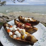 3 campfire banana boats. One is stuffed with reeses pieces peanut butter cups and marshmallows, another with marshmallows, strawberries and chocolate chips, and the final one with marshmallows, chocolate chips, and golden grahams cereal.