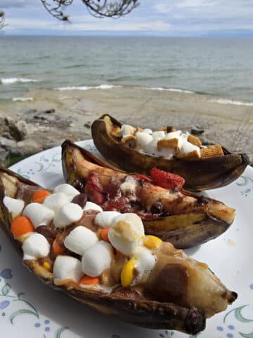 3 campfire banana boats. One is stuffed with reeses pieces peanut butter cups and marshmallows, another with marshmallows, strawberries and chocolate chips, and the final one with marshmallows, chocolate chips, and golden grahams cereal.