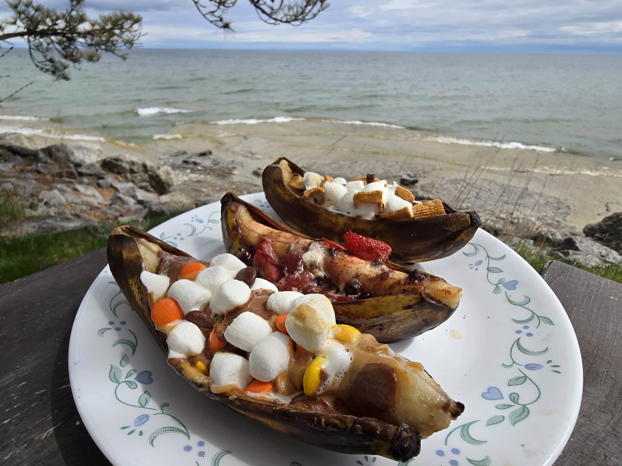 3 campfire banana boats.  One is stuffed with reeses pieces peanut butter cups and marshmallows, another with marshmallows, strawberries and chocolate chips, and the final one with marshmallows, chocolate chips, and golden grahams cereal.