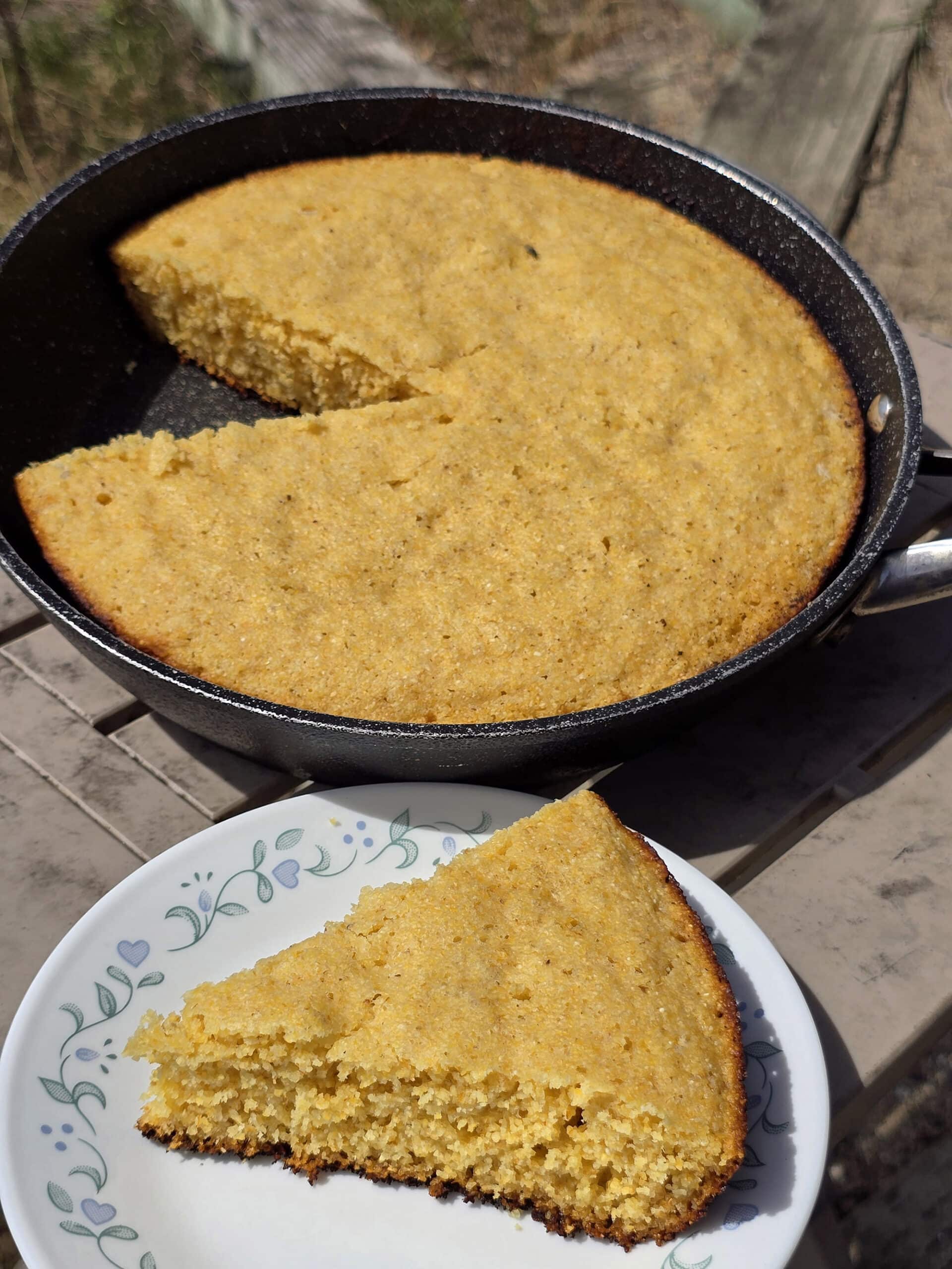 A pan of skillet cornbread next to a plate with a wedge of cornbread.