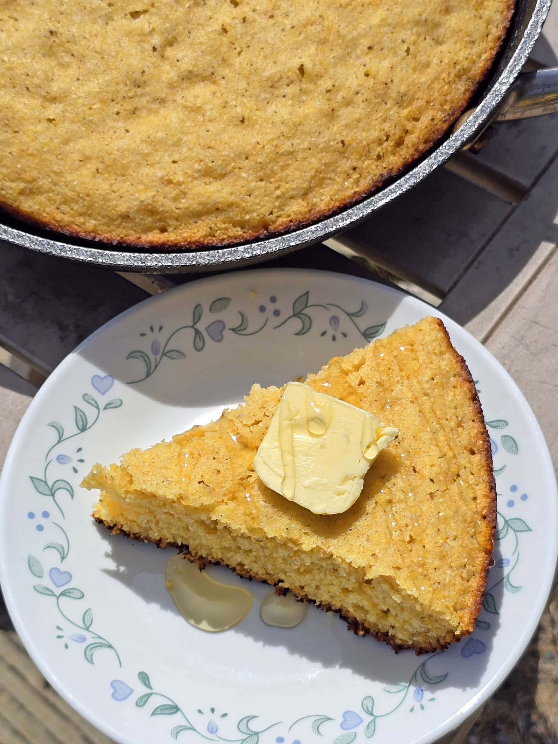 A pan of skillet campfire cornbread next to a plate with a wedge of cornbread.