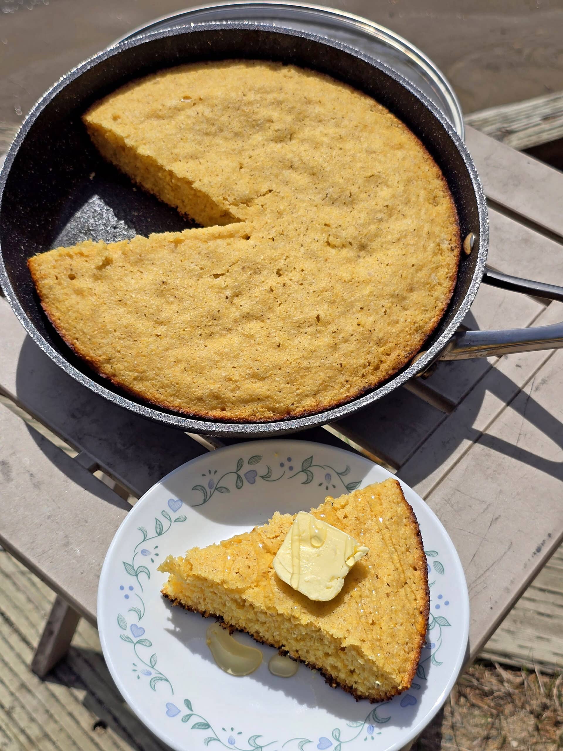 A pan of skillet cornbread next to a plate with a wedge of cornbread.