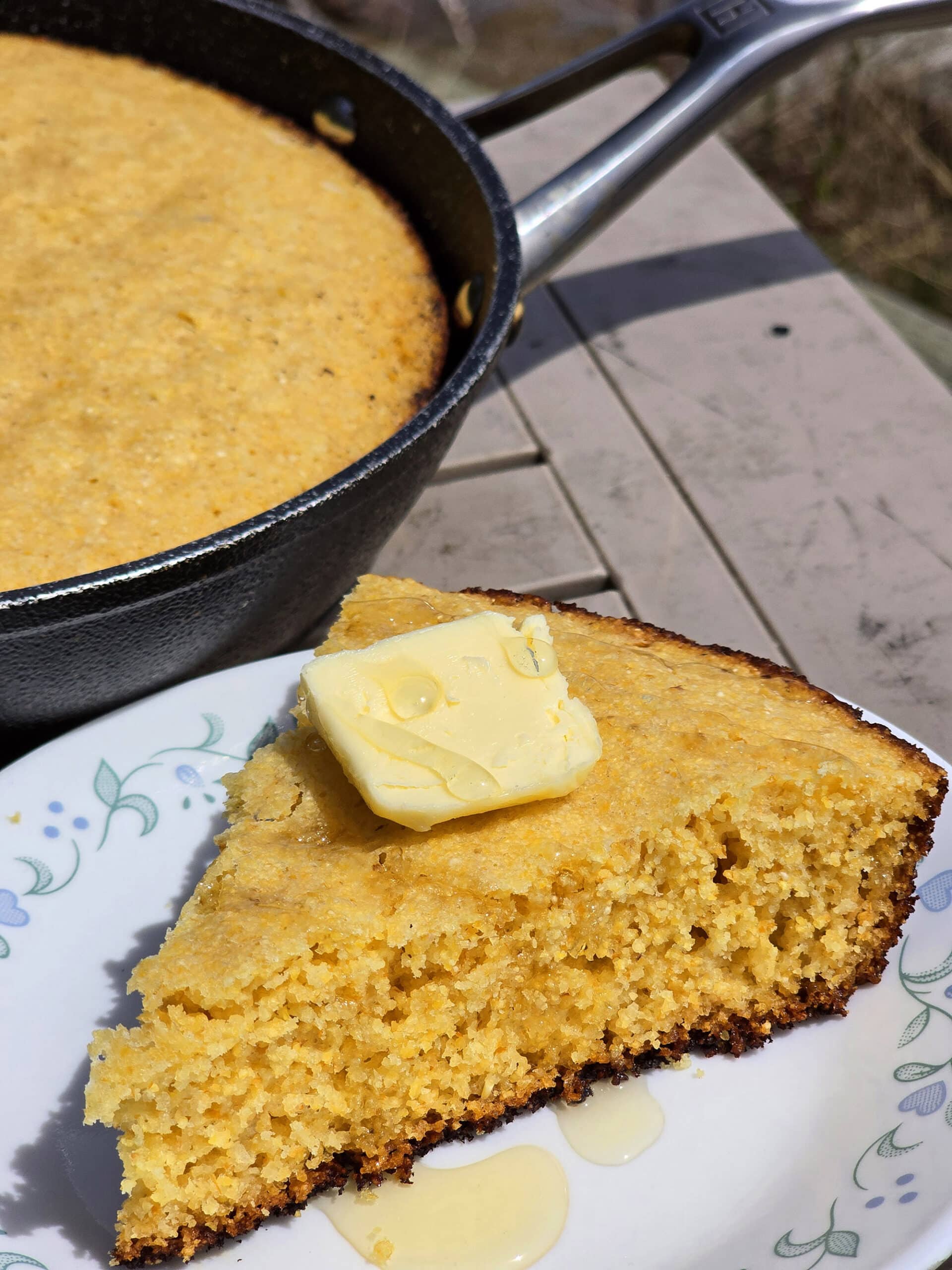A pan of skillet campfire cornbread next to a plate with a wedge of cornbread.