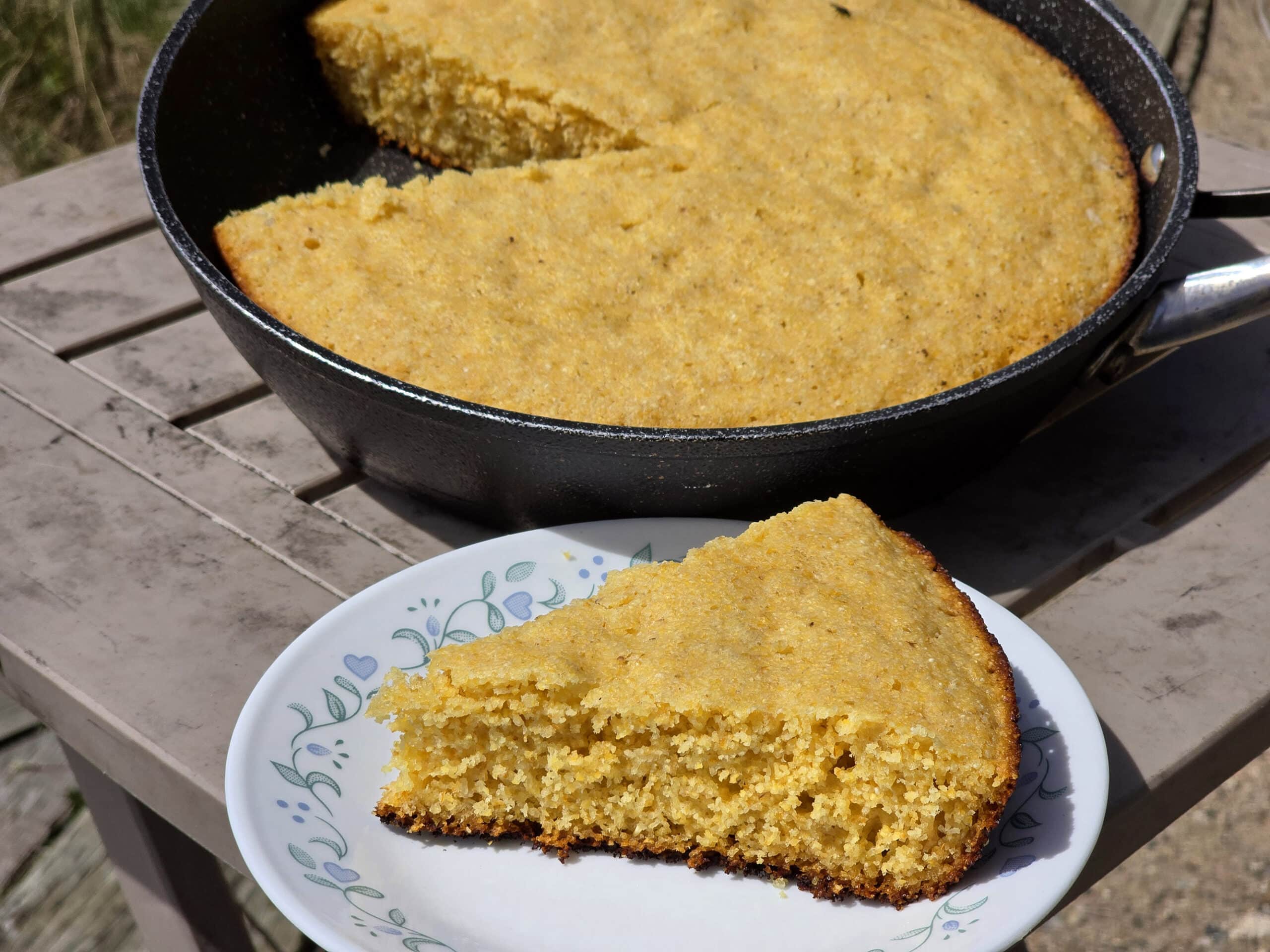 A pan of skillet cornbread next to a plate with a wedge of cornbread.