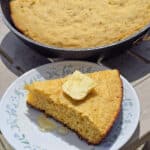 A pan of skillet campfire cornbread next to a plate with a wedge of cornbread.