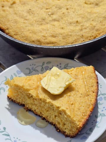 A pan of skillet campfire cornbread next to a plate with a wedge of cornbread.