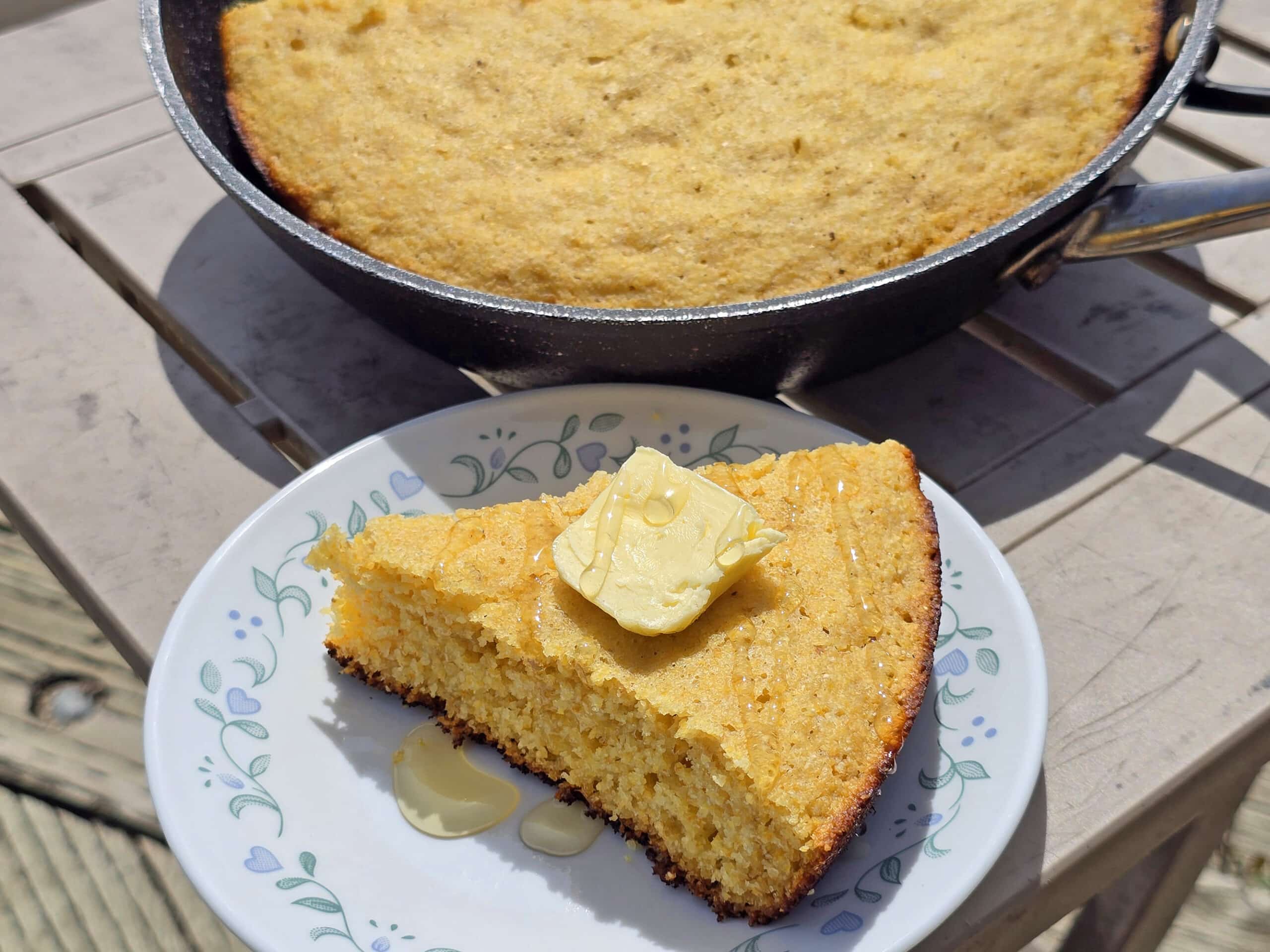 A pan of skillet campfire cornbread next to a plate with a wedge of cornbread.