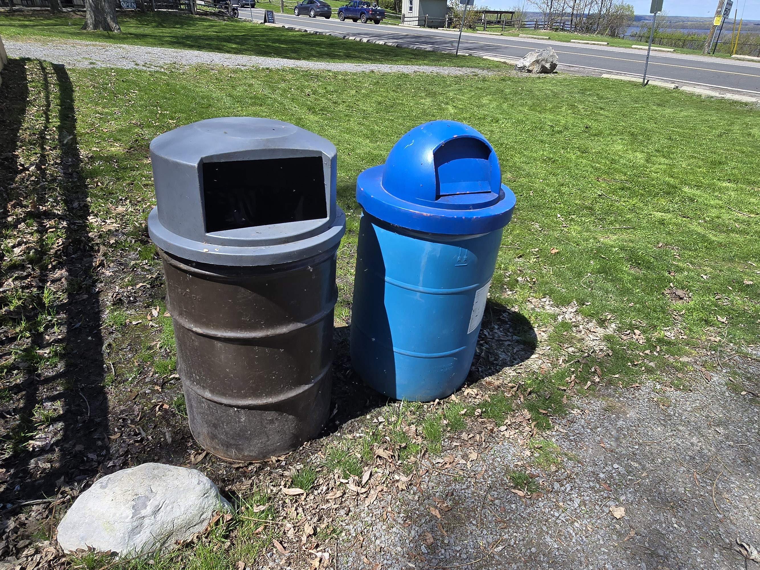 Two garbage cans on the side of a path.