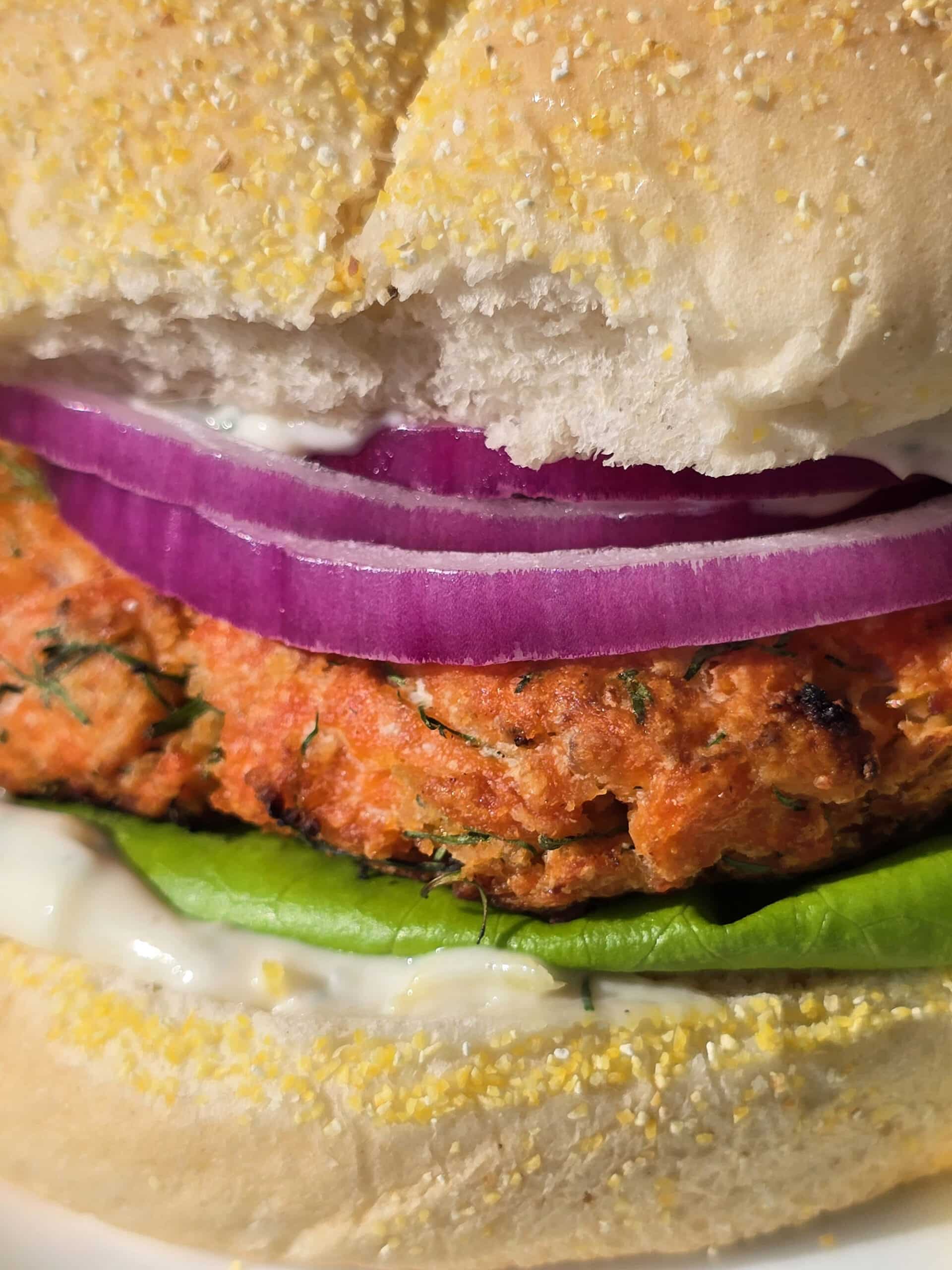 A Lemon dill fresh salmon burger with lettuce, lemon dill mayonnaise, and red onions.
