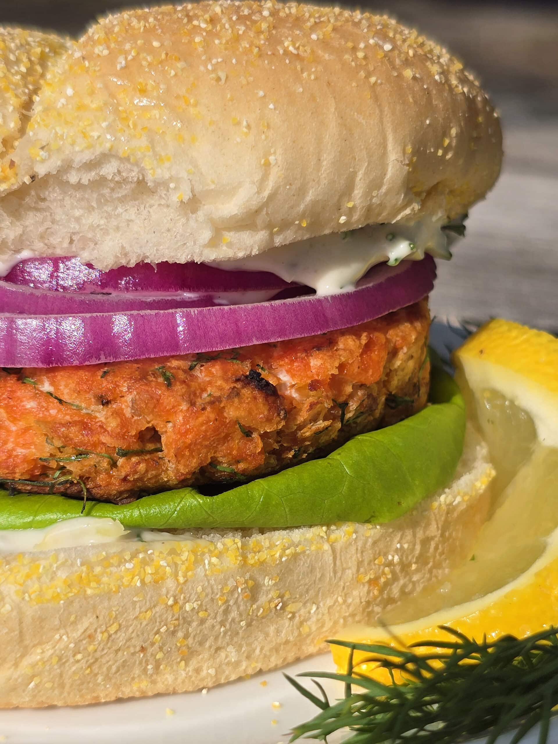 A Lemon dill salmon burger with lettuce, lemon dill mayonnaise, and red onions.