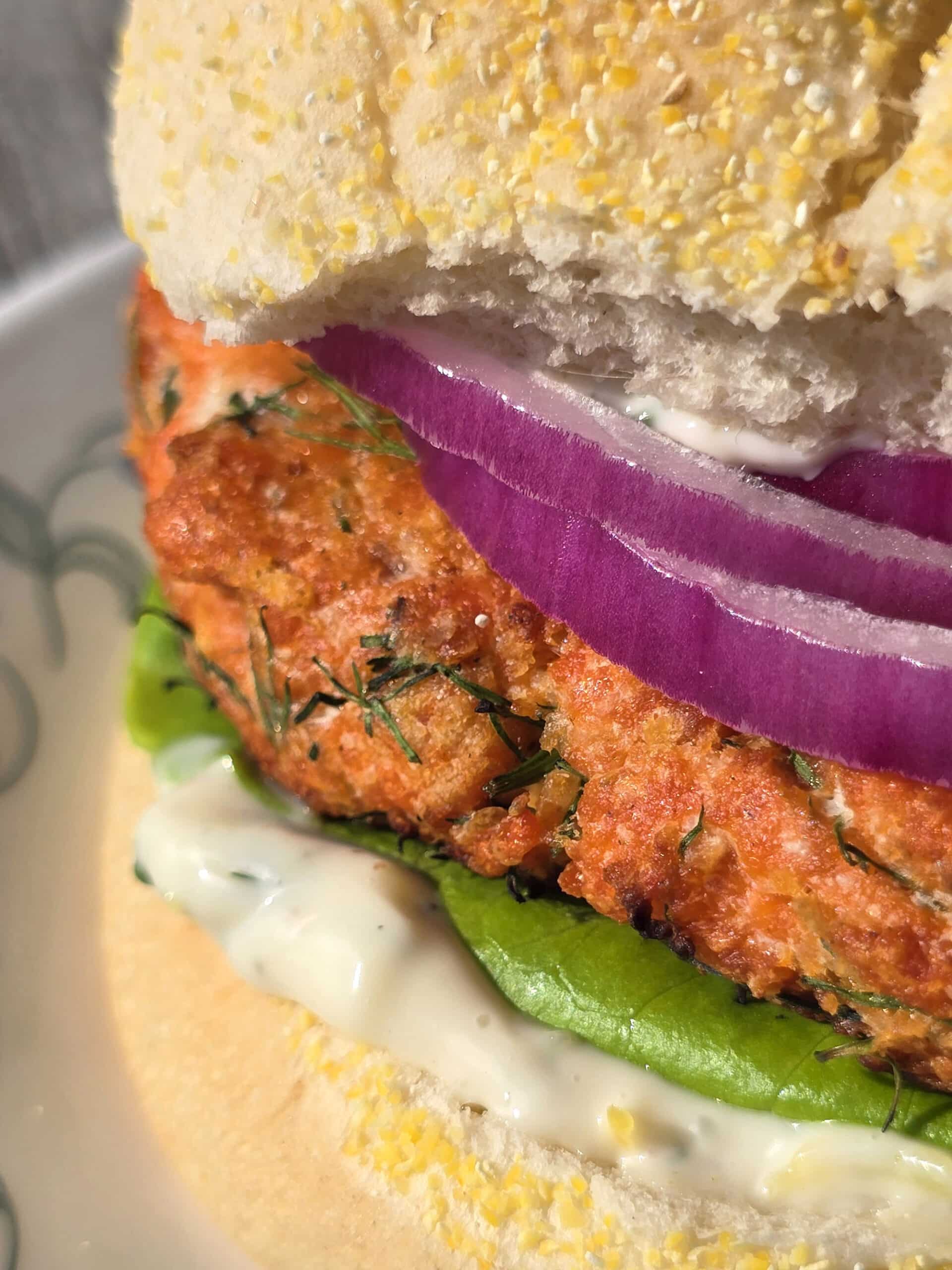 A Lemon dill salmon burger with lettuce, lemon dill mayonnaise, and red onions.