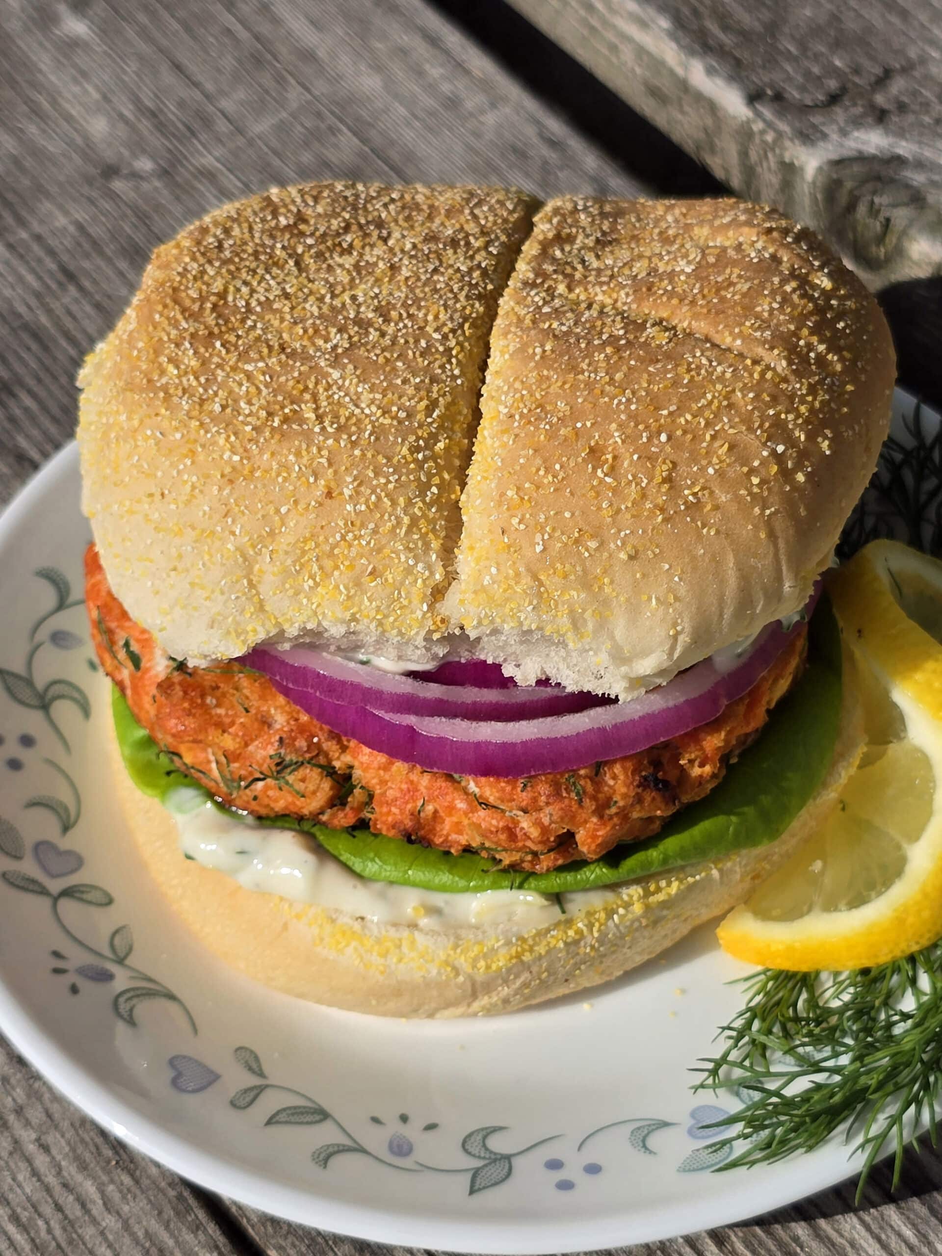 A Lemon dill fresh salmon burger with lettuce, lemon dill mayonnaise, and red onions.