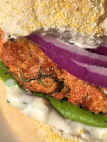 A Lemon dill salmon burger with lettuce, lemon dill mayonnaise, and red onions.