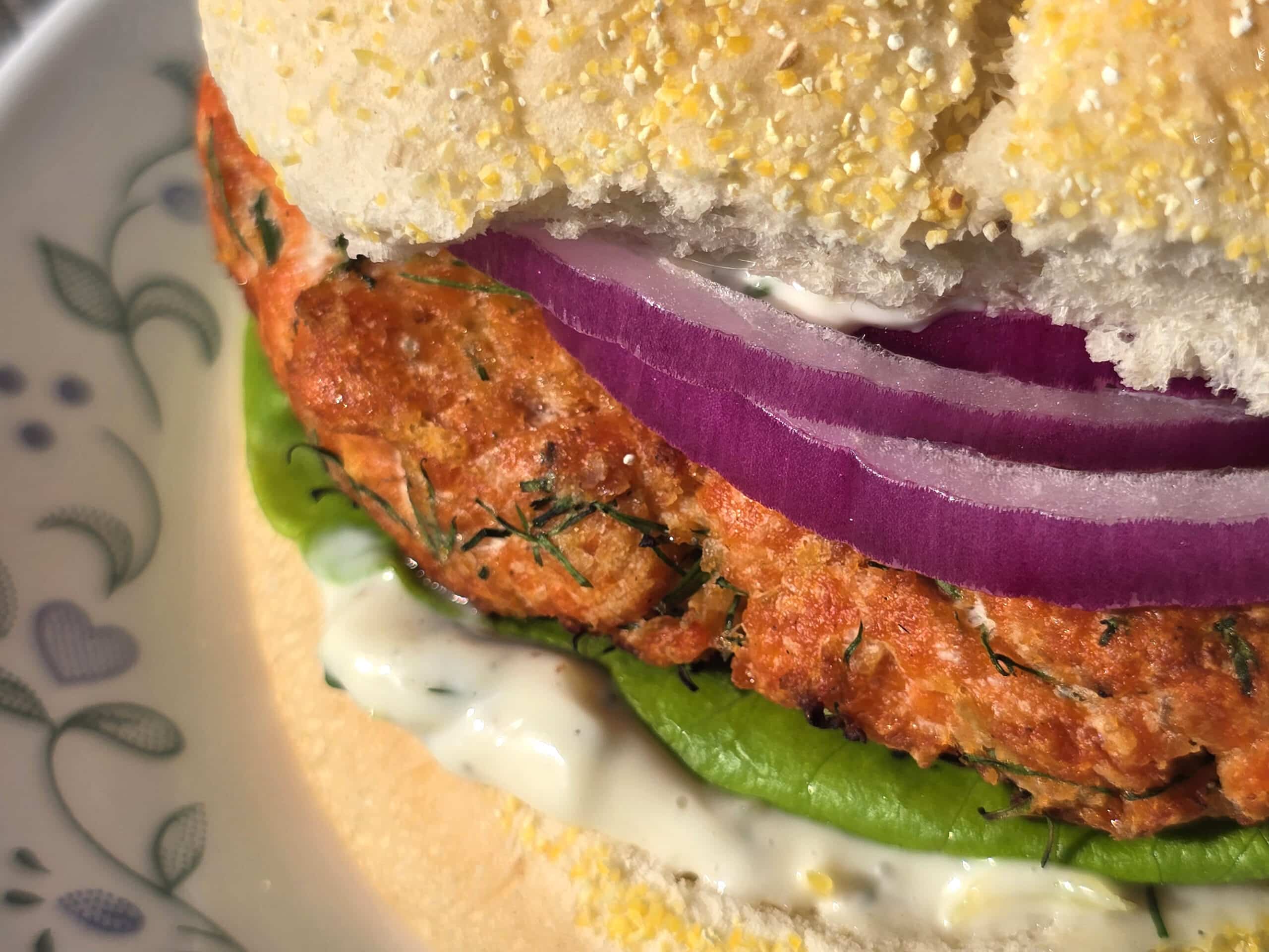A Lemon dill salmon burger with lettuce, lemon dill mayonnaise, and red onions.