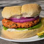 A Lemon dill fresh salmon burger with lettuce, lemon dill mayonnaise, and red onions.