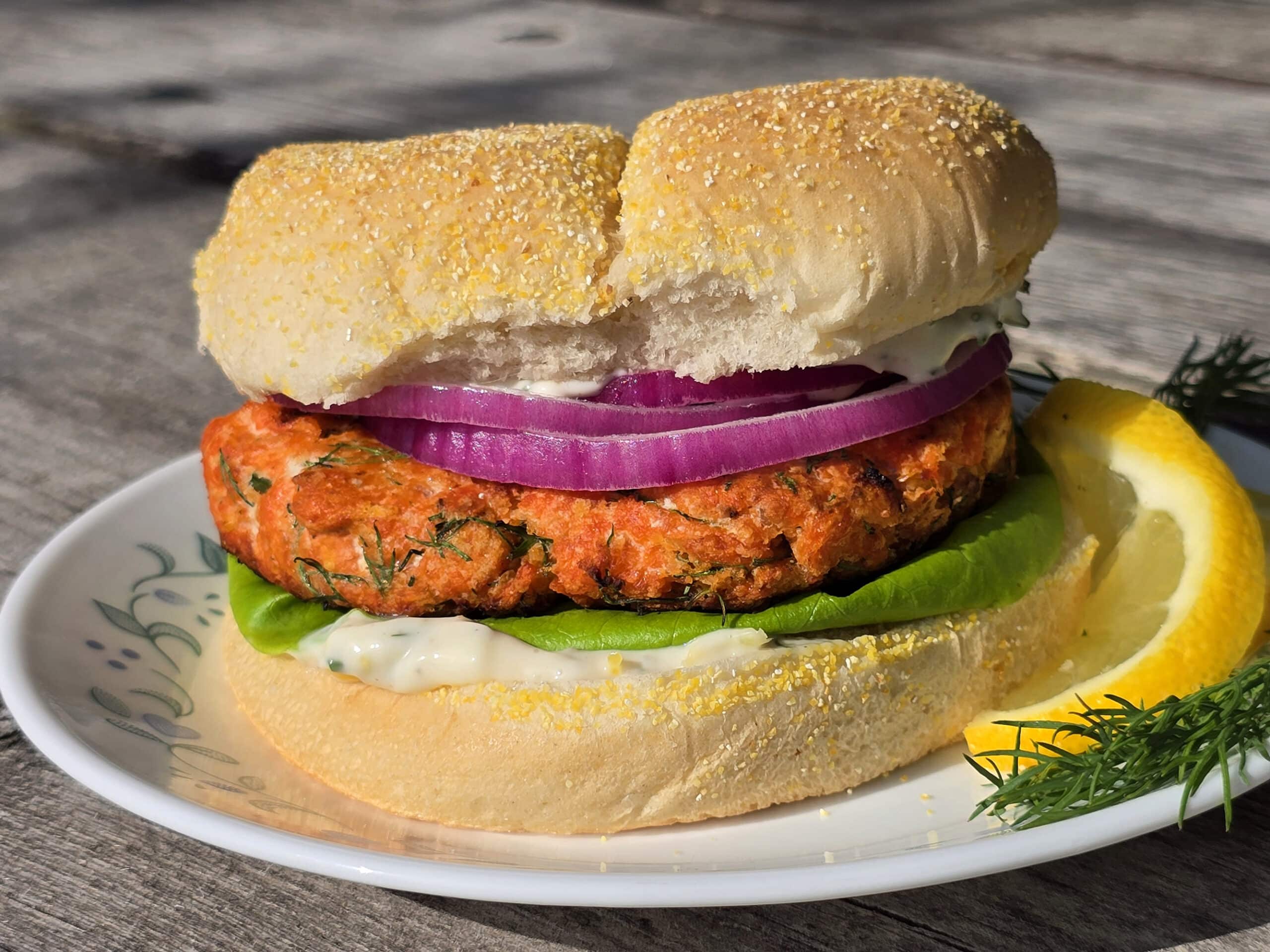 A Lemon dill fresh salmon burger with lettuce, lemon dill mayonnaise, and red onions.