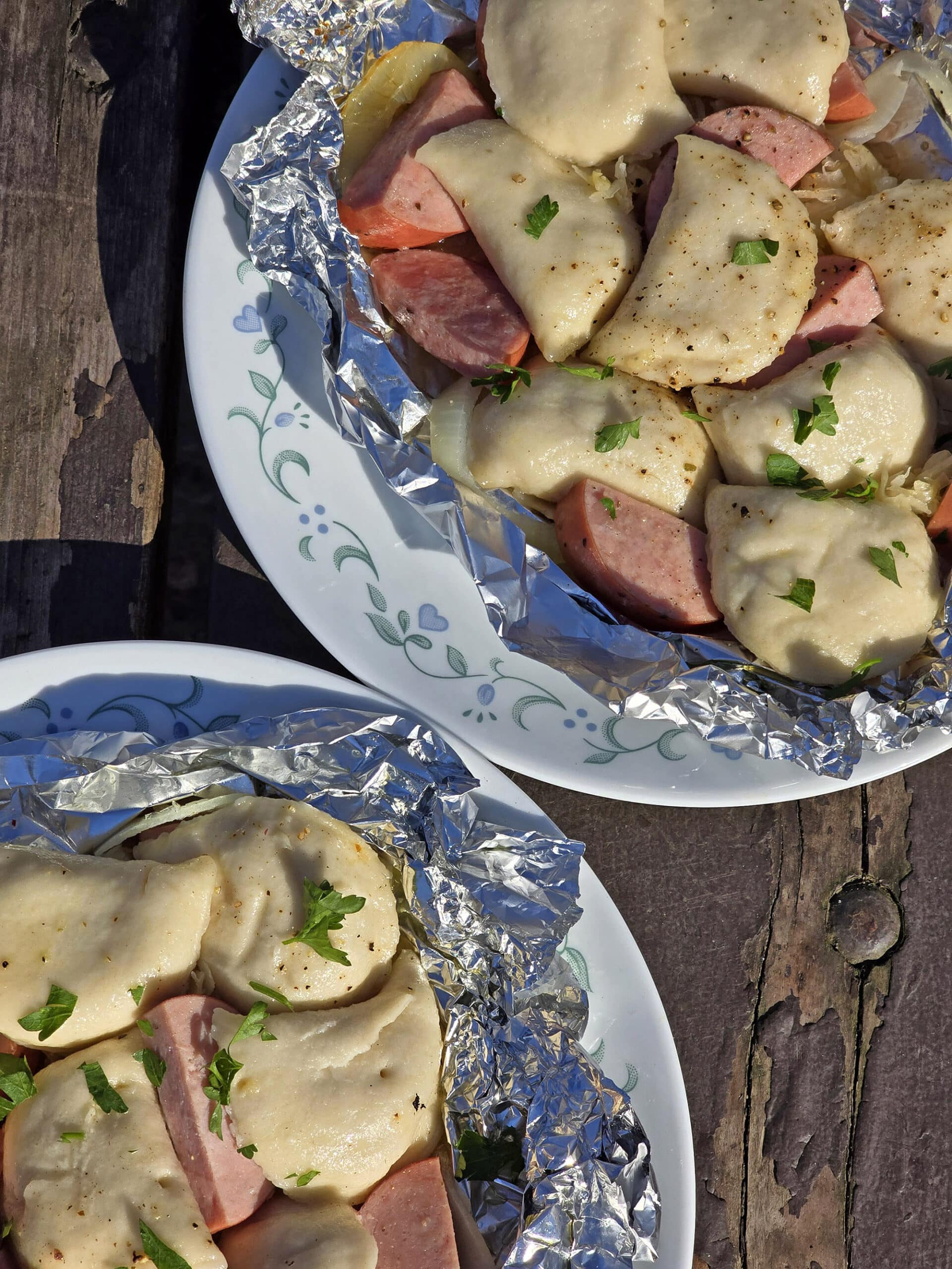 2 pierogi and kielbasa foil packets on a campground picnic table.