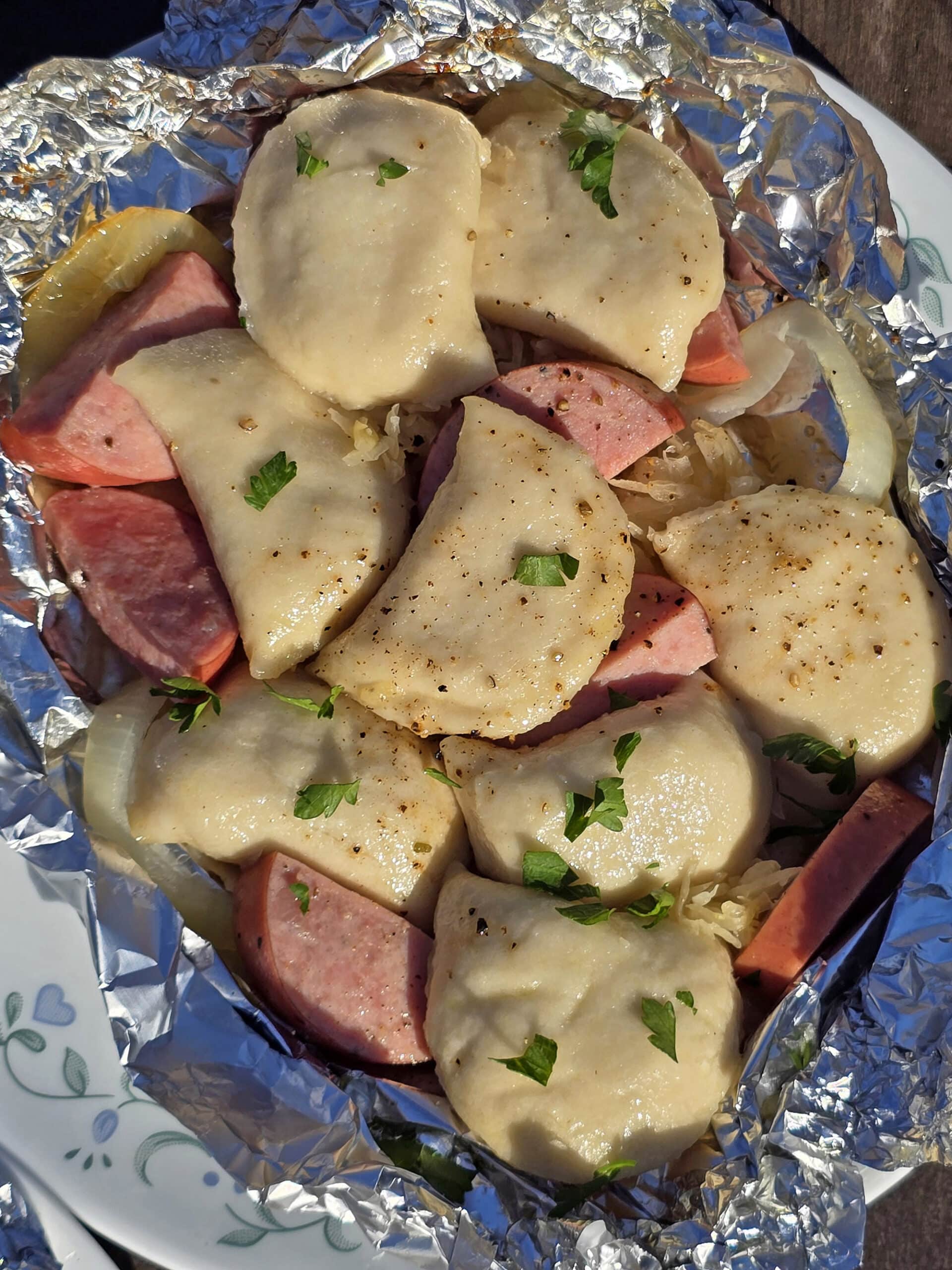 A pierogi and kielbasa foil packet on a campground picnic table.