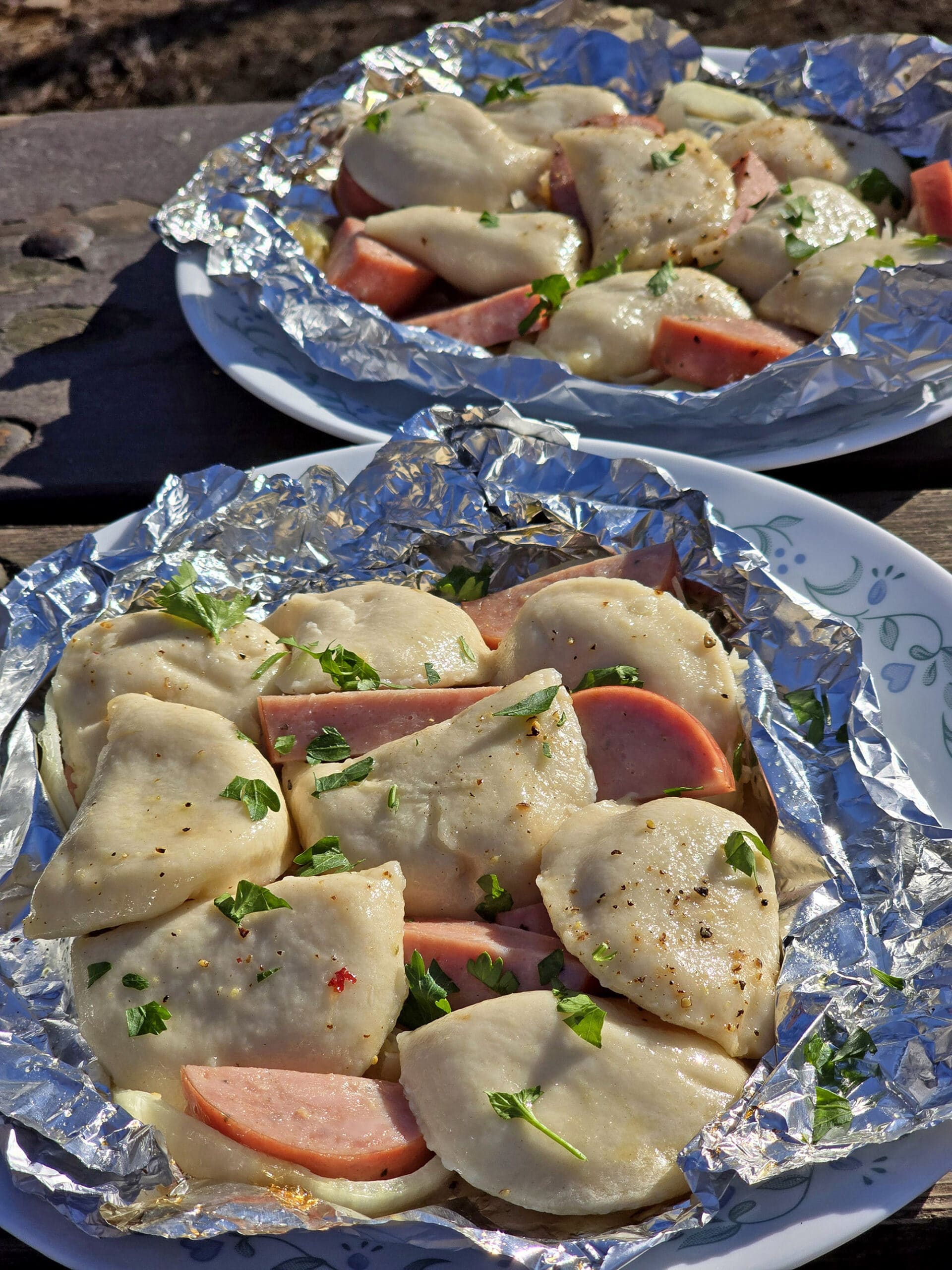 2 pierogi and kielbasa foil packets on a campground picnic table.