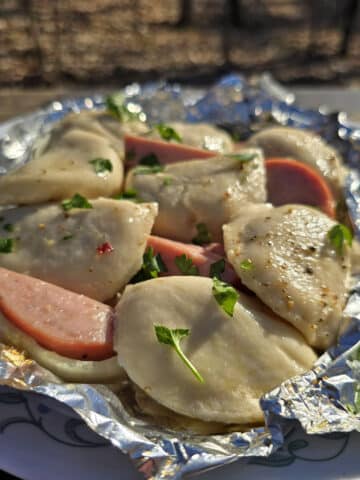 A pierogi and kielbasa foil packet on a campground picnic table.