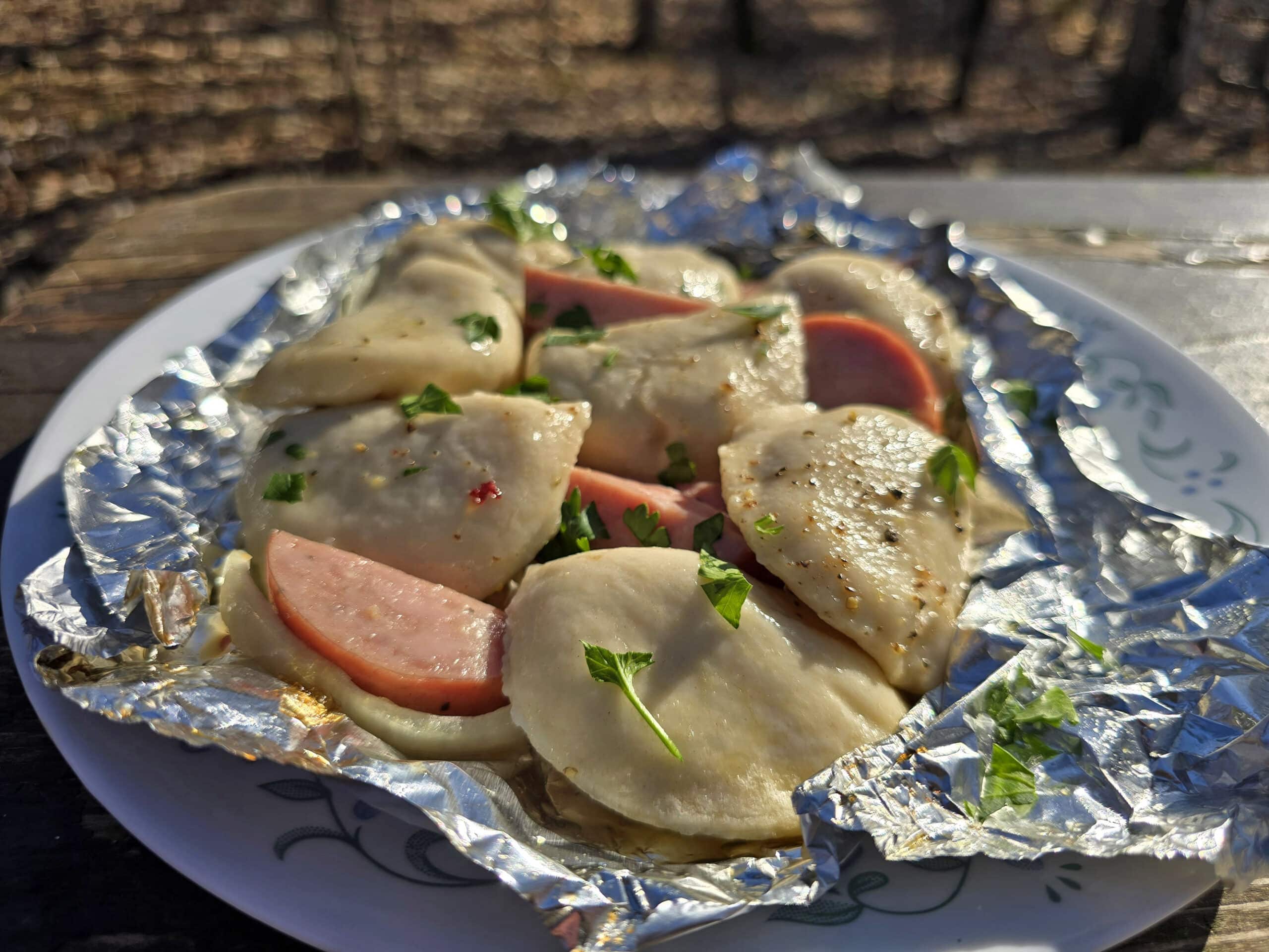 A pierogi and kielbasa foil packet on a campground picnic table.