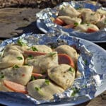 2 foil packets of steamed perogies and sausage on a campground picnic table.