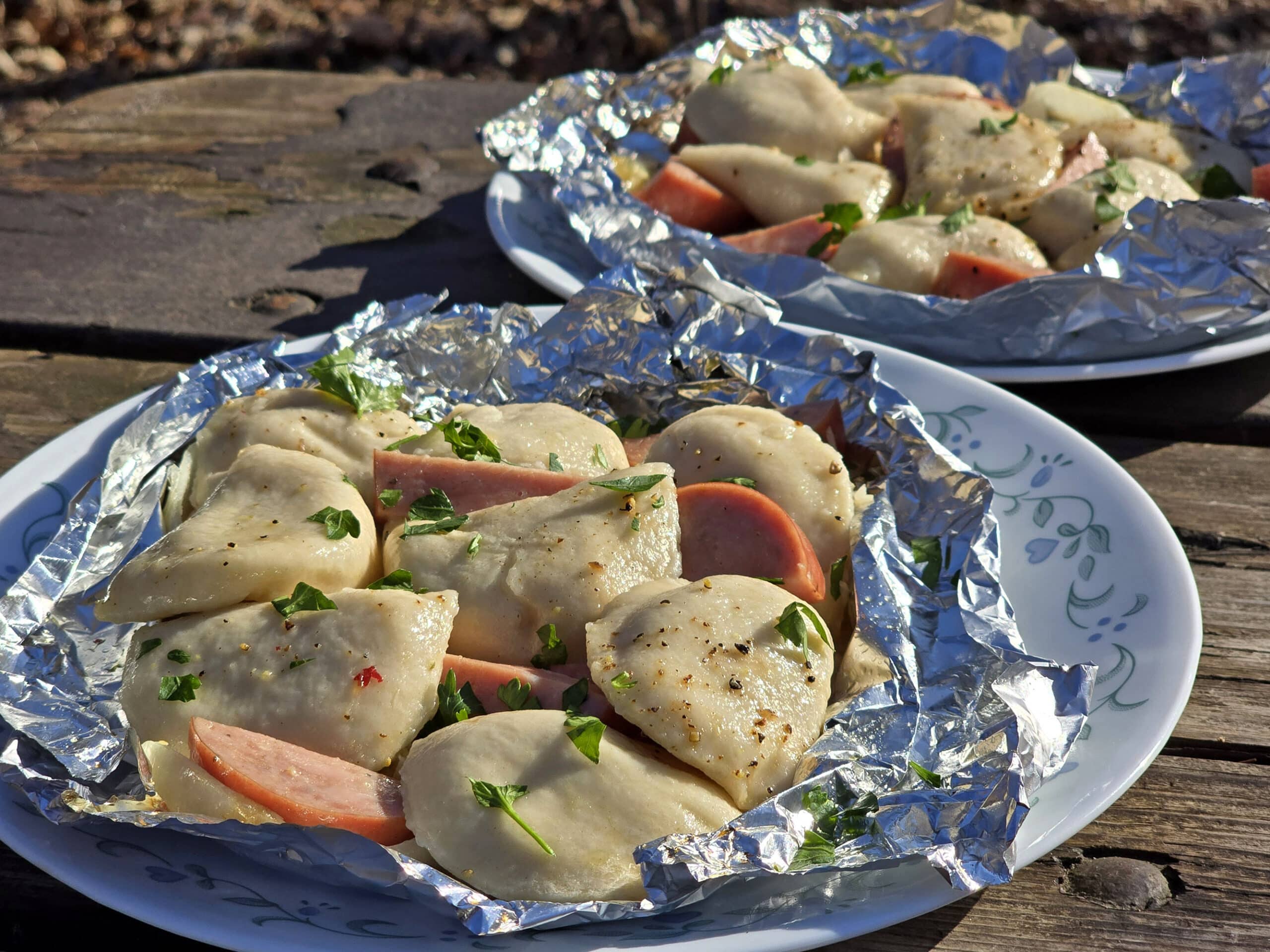 2 foil packets of steamed perogies and sausage on a campground picnic table.