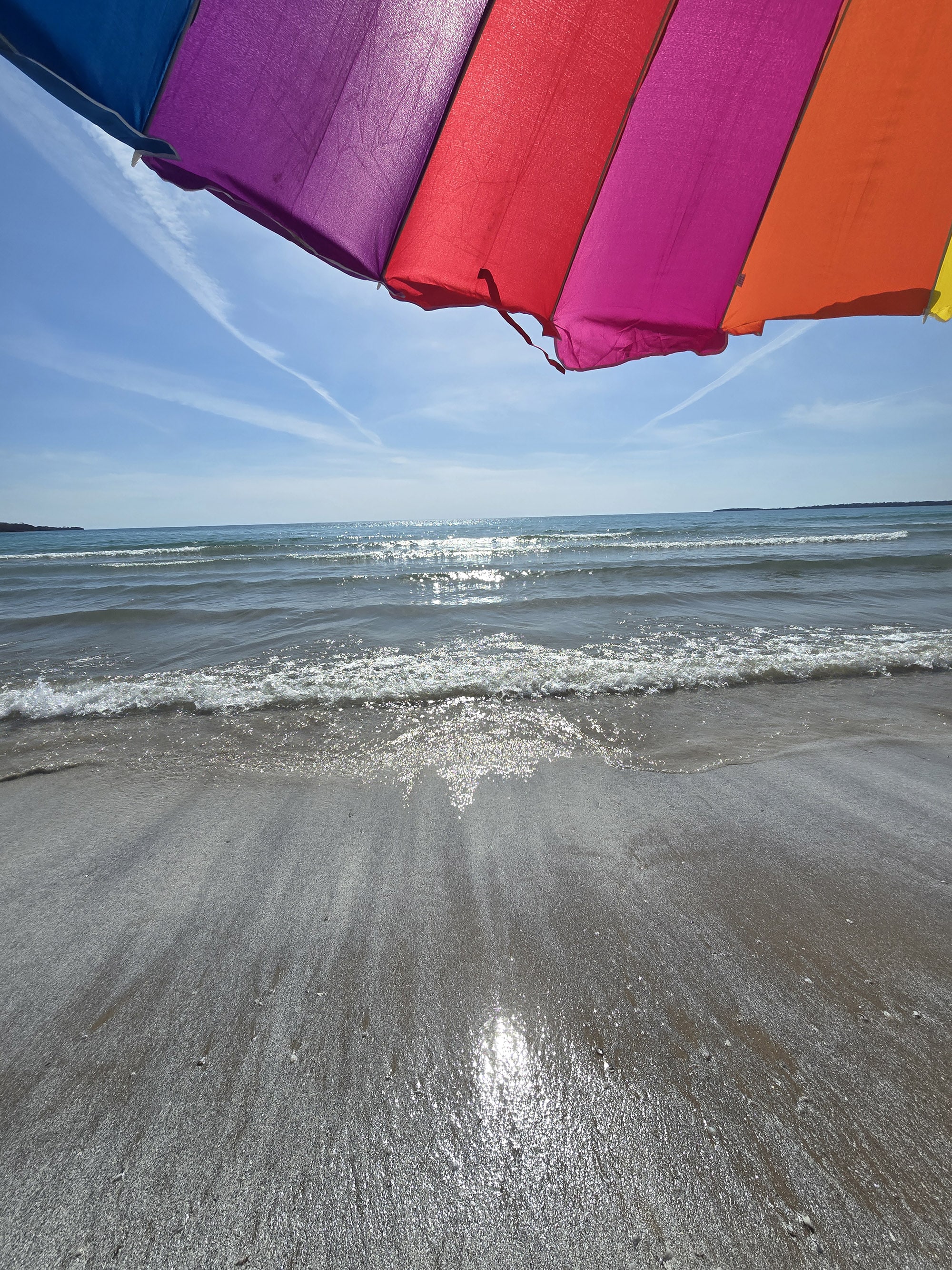 Sandbanks Beach on a sunny day, with a rainbow umbrella overhead.