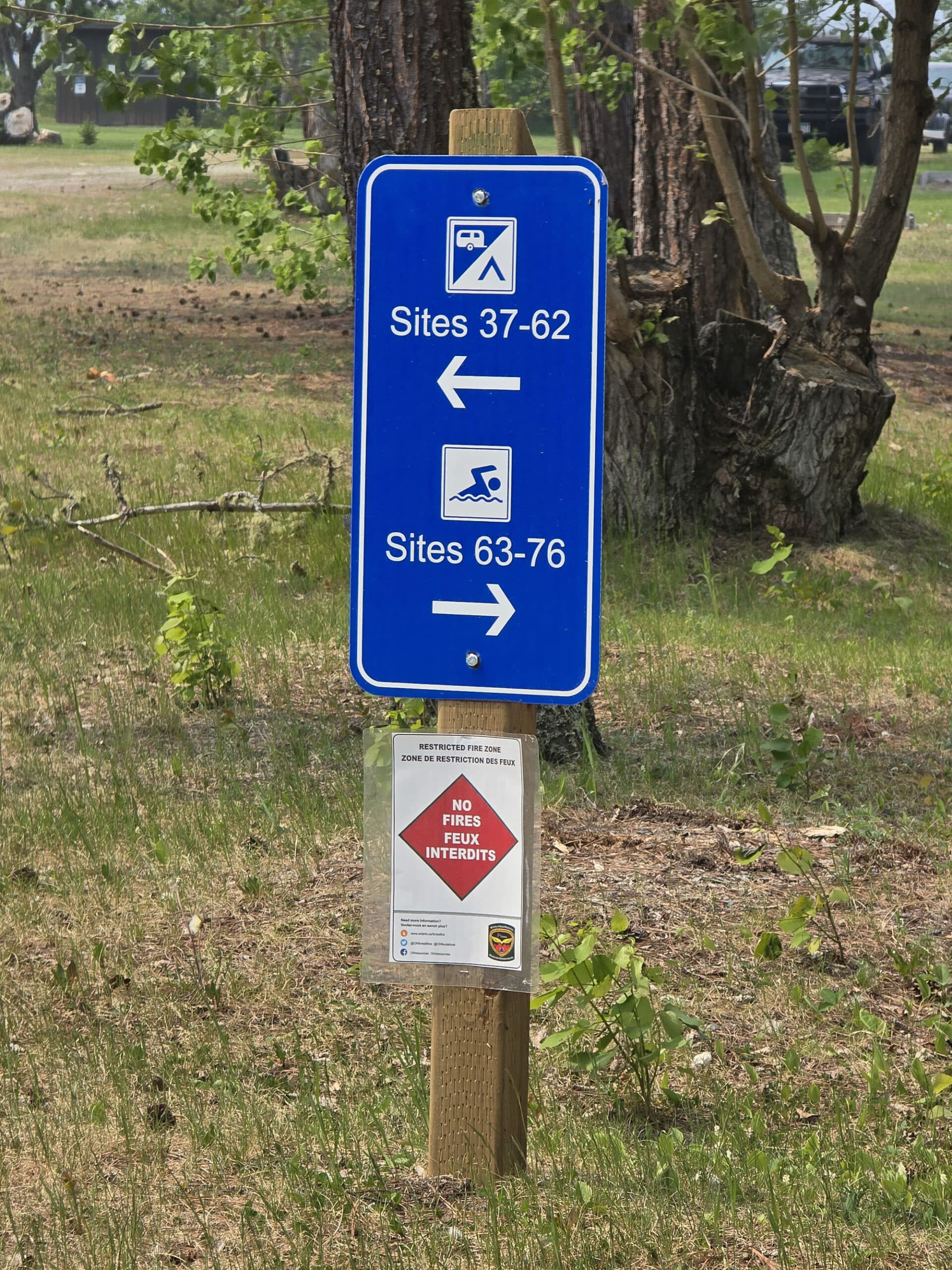 A blue road sign with graphics and numbers indicating where to find groups of campsites and the beach at Pakwash Provincial Park.