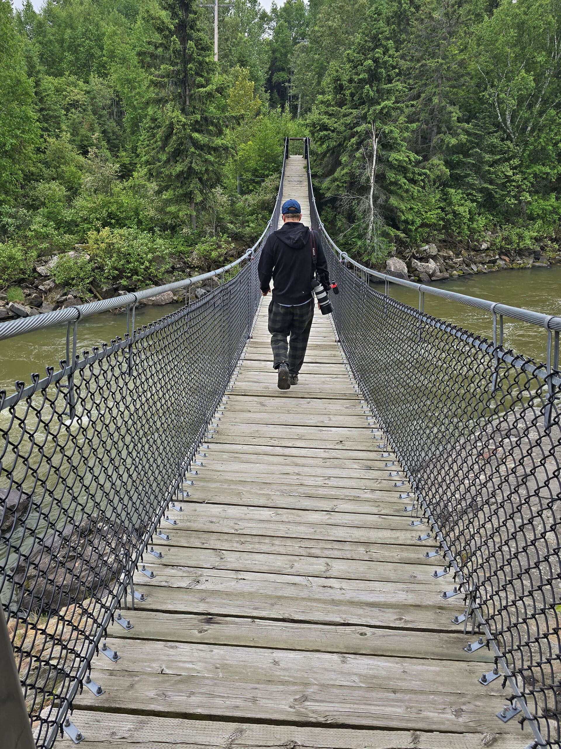 A man walking across the roy wilson suspension bridge.