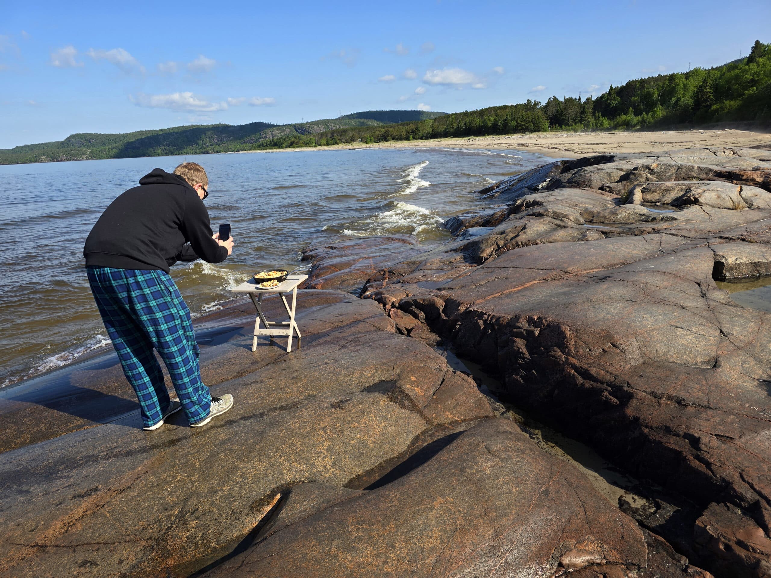 A man photographing a pan of bagel breakfast strata on the beach at Neys Provincial Park