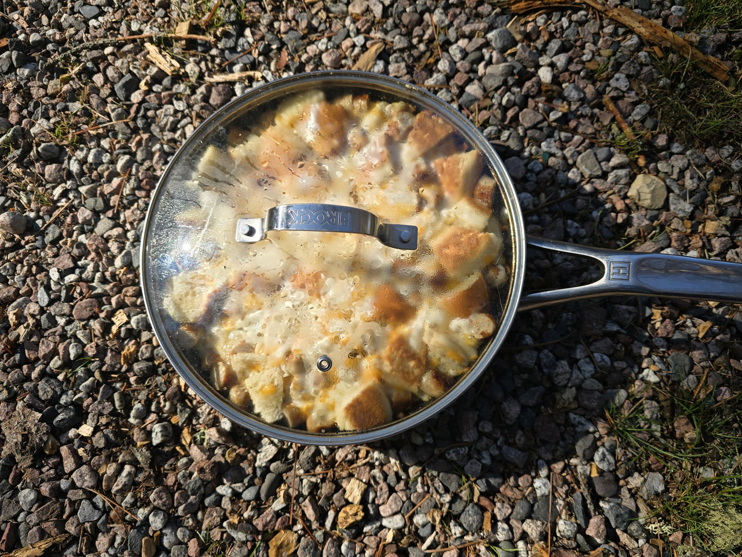 A covered skillet of bagel breakfast strata resting on gravel.