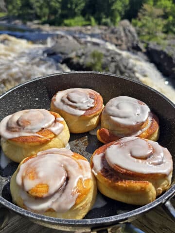 A skillet of frosted campfire cinnamon rolls next to a waterfall.