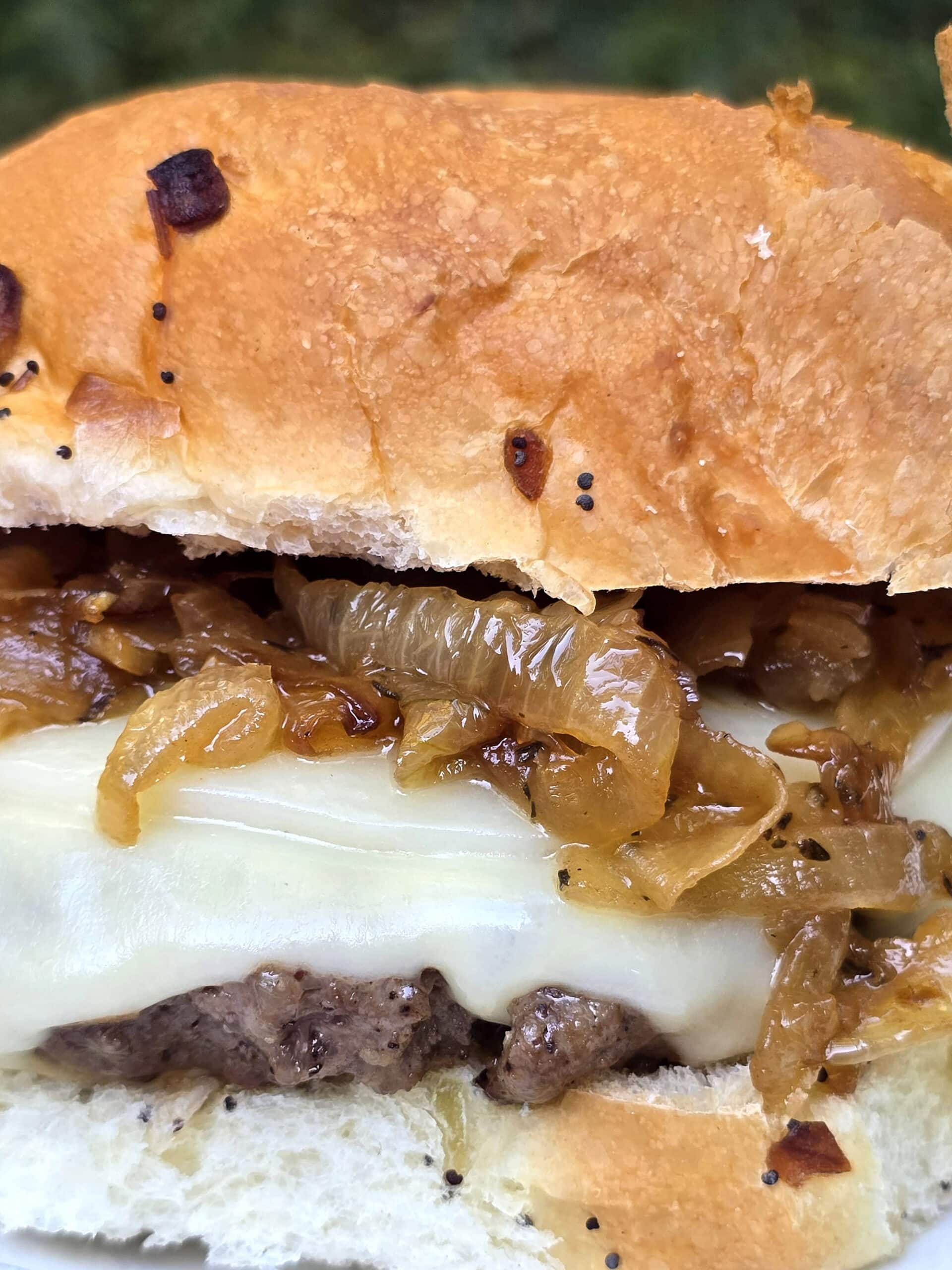 A French onion soup burger on a plate, with provolone, swiss, and caramelized onions.