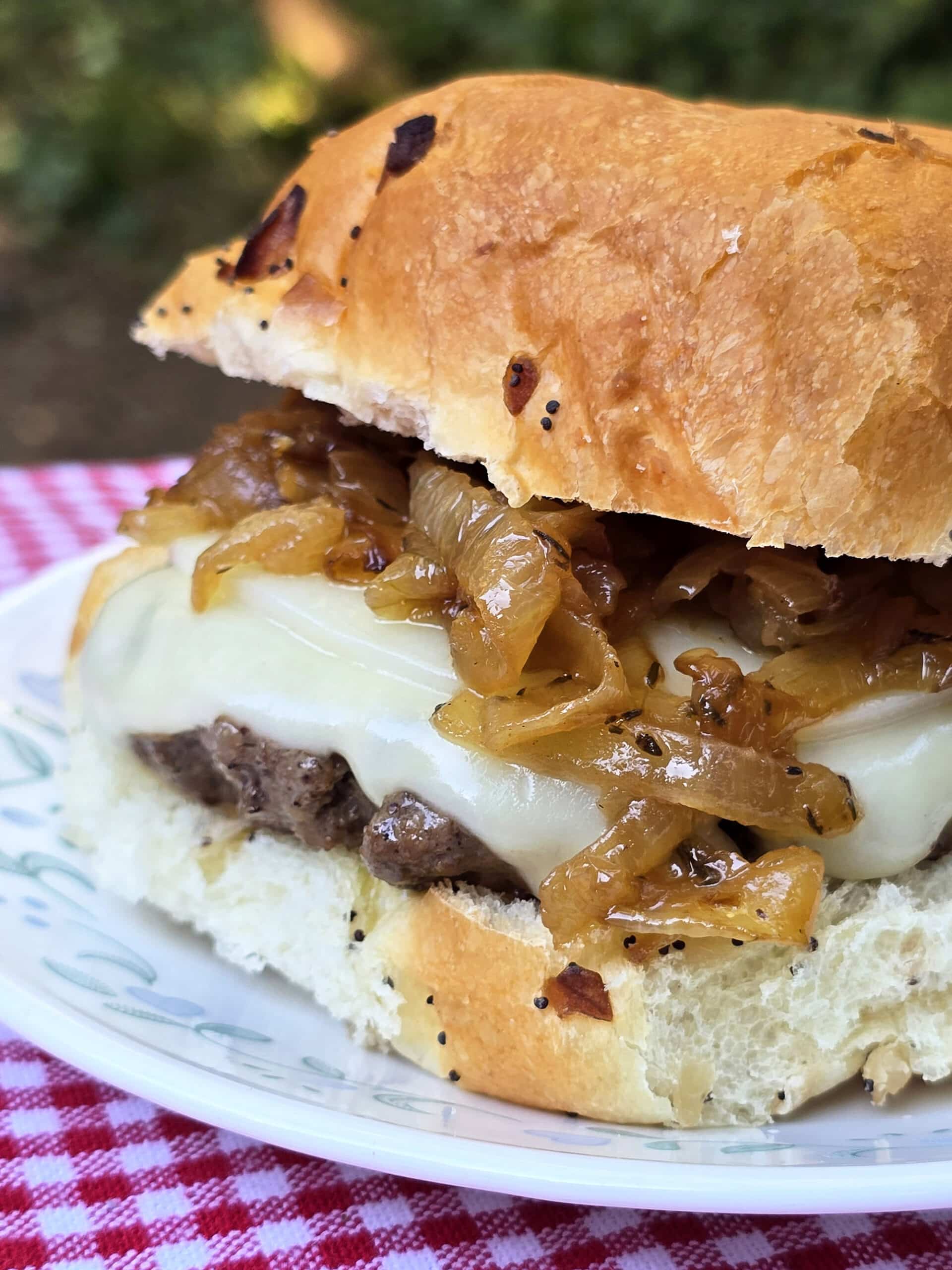 A French onion soup cheeseburger on a plate, with provolone, swiss, and caramelized onions.