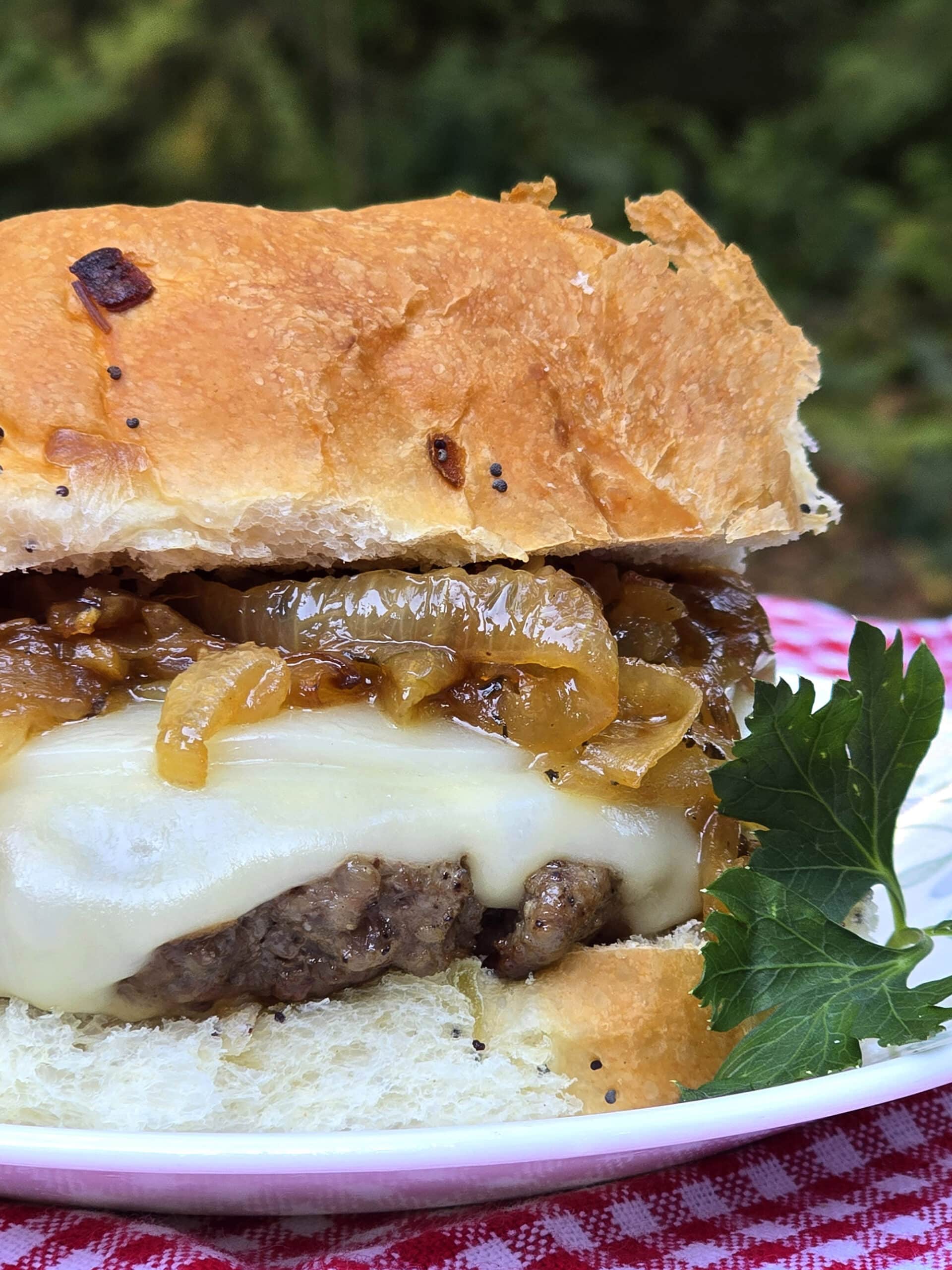 A French onion soup burger on a plate, with provolone, swiss, and caramelized onions.