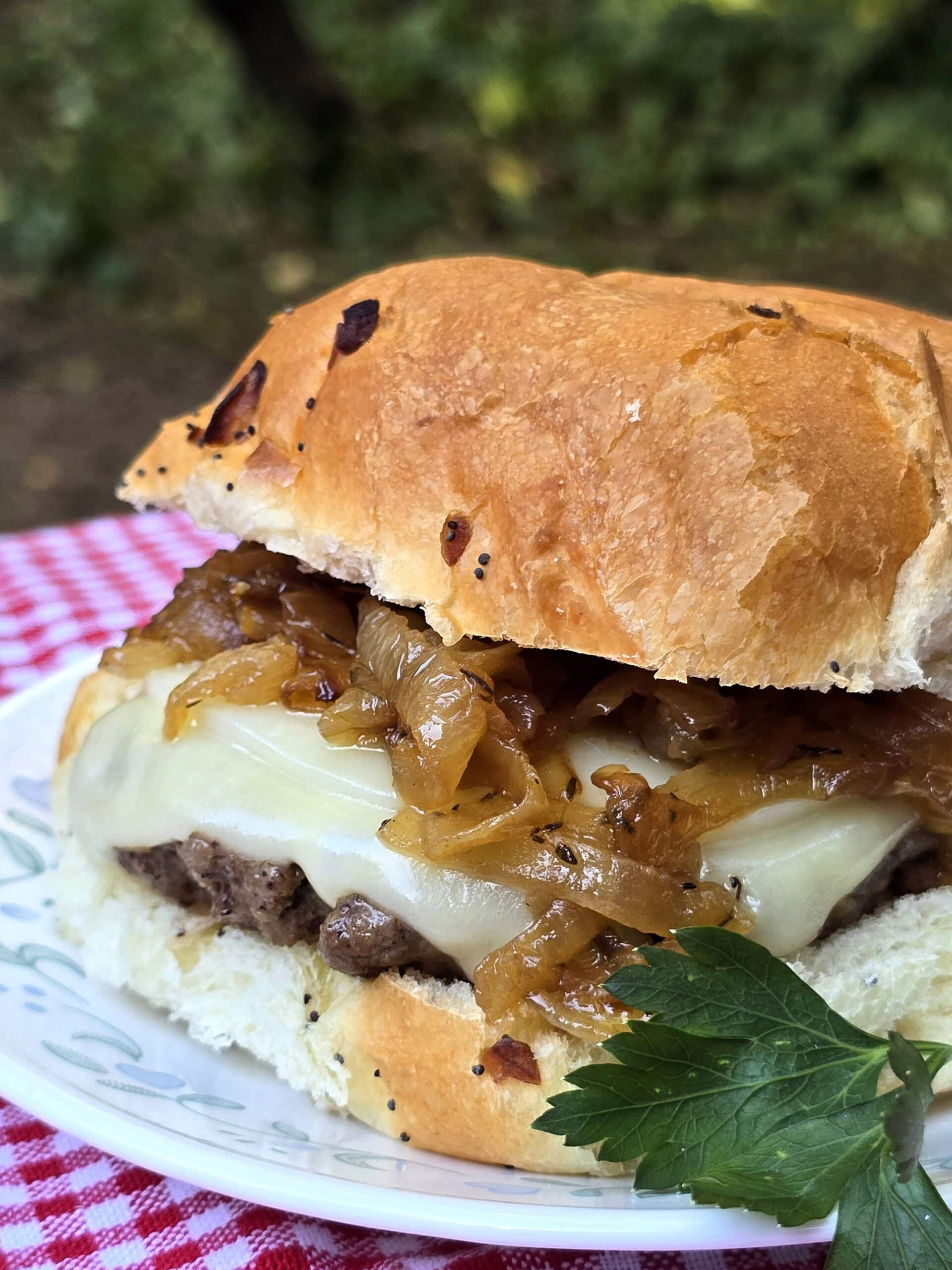 A French onion soup cheeseburger on a plate, with provolone, swiss, and caramelized onions.