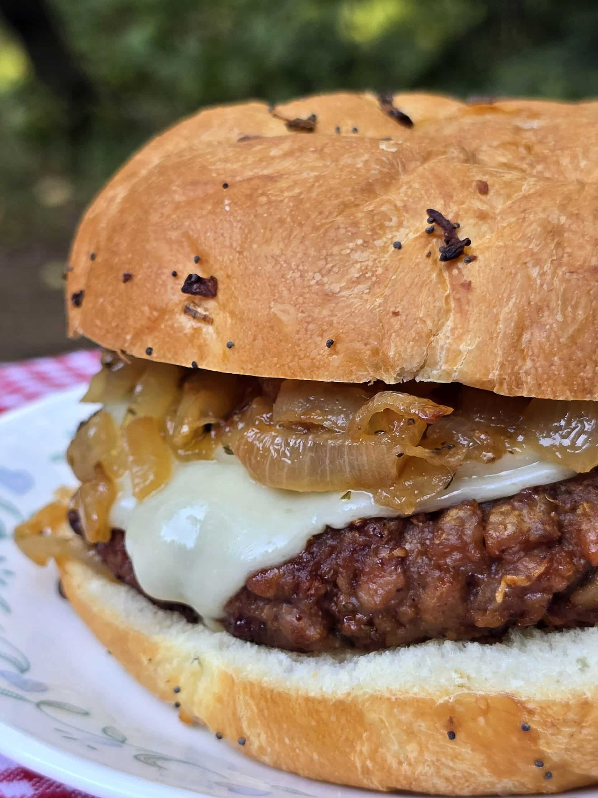 A French onion soup burger on a plate, with provolone, swiss, and caramelized onions.
