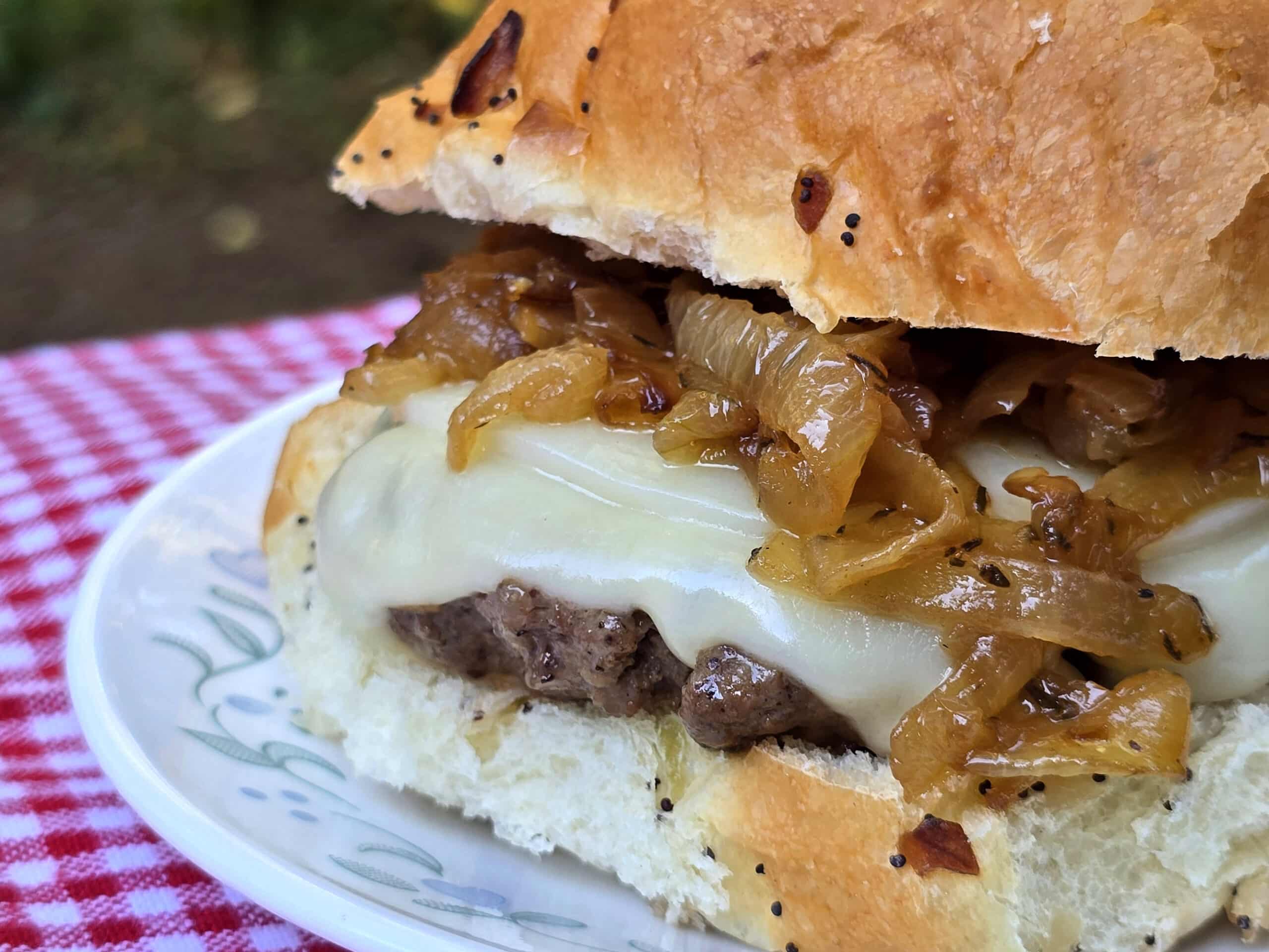 A French onion soup cheeseburger on a plate, with provolone, swiss, and caramelized onions.